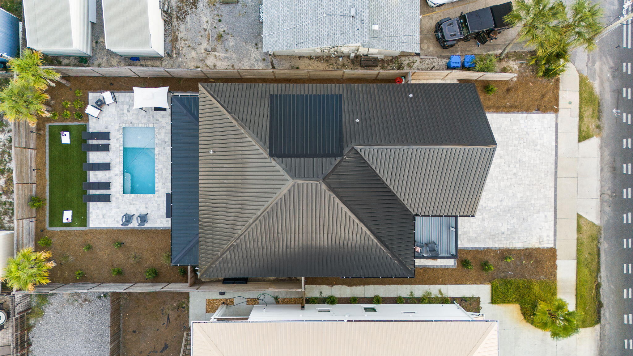 Aerial view of a dark-roofed home with a fenced pool and stone patio.