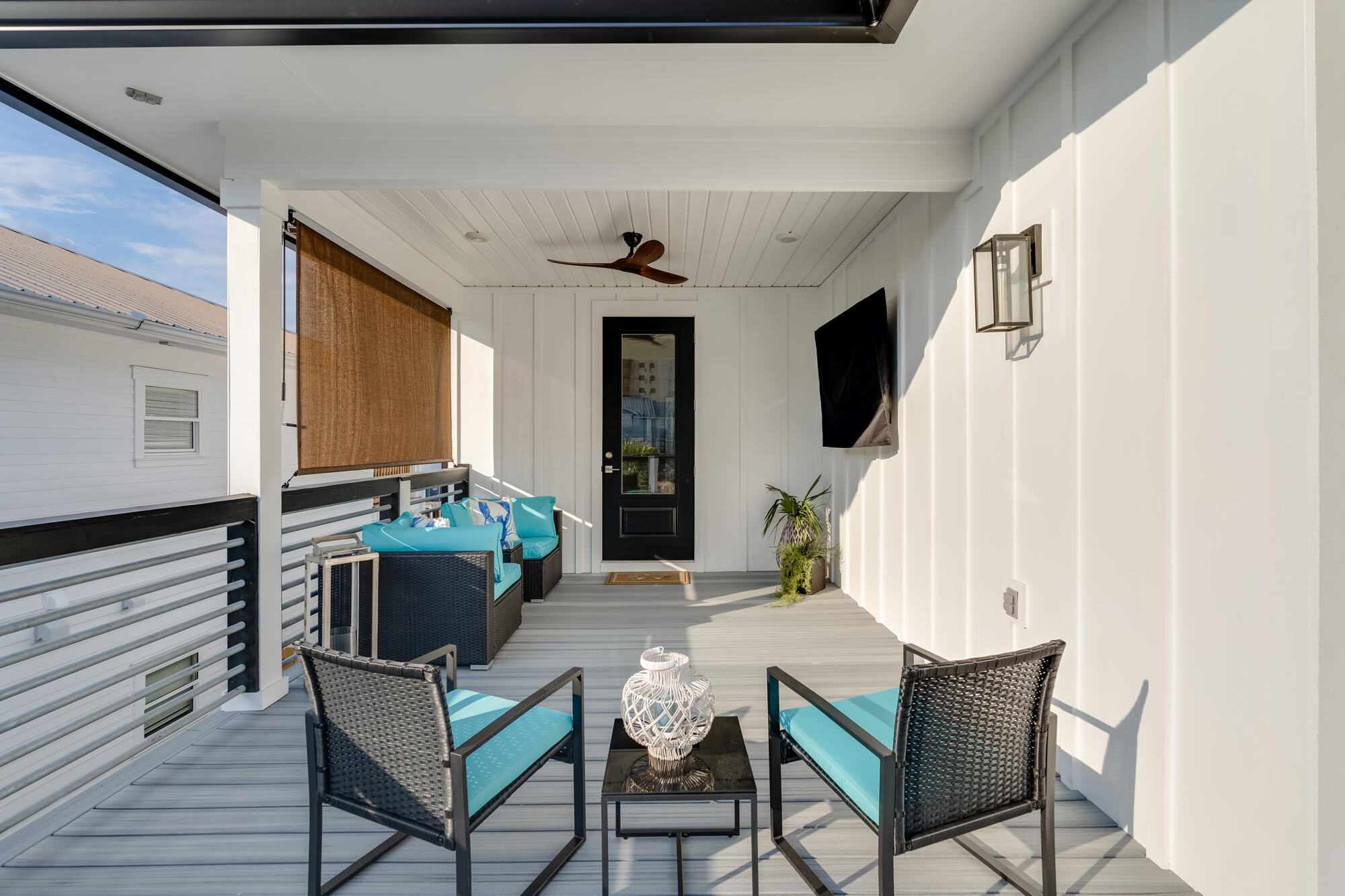 Covered porch with turquoise-cushioned wicker seating, a ceiling fan, and a wall-mounted television.