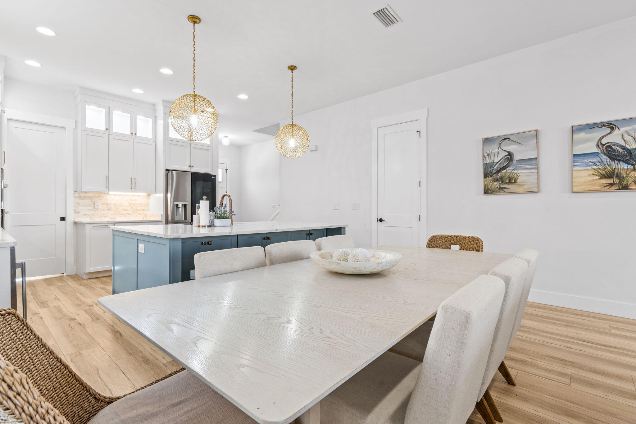 Kitchen and dining area with a blue island, white table, and gold pendant lights.