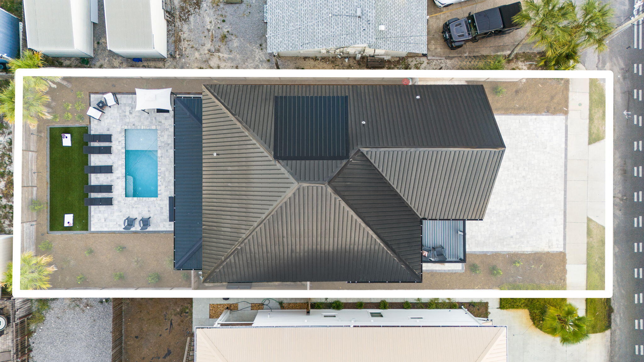 Aerial view of a dark-roofed house with a backyard pool and paved patio.