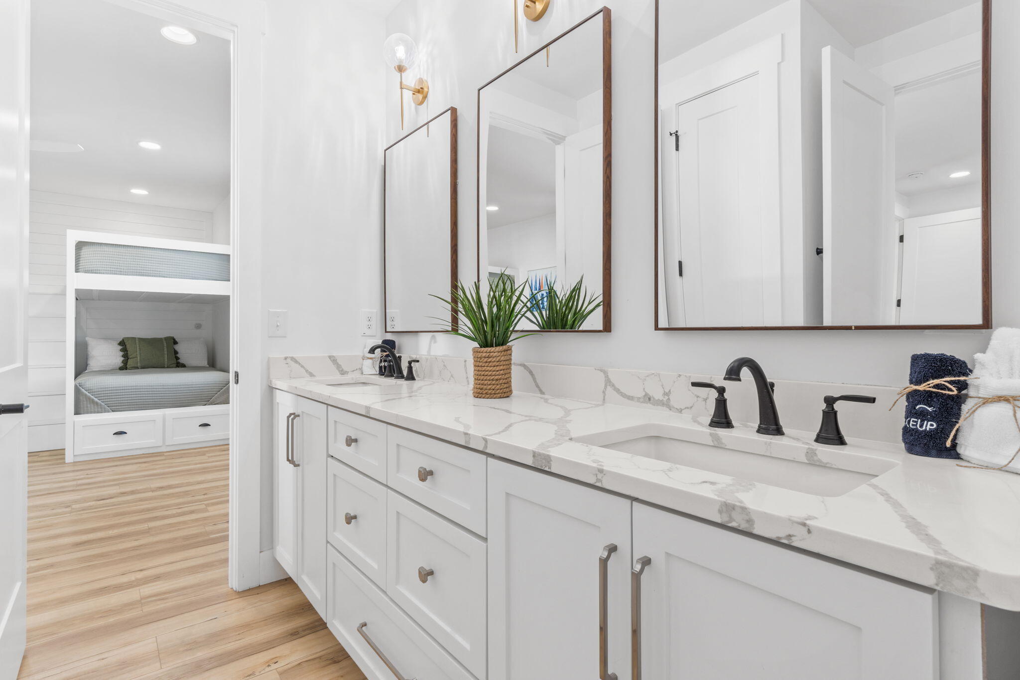 Bathroom double vanity with marble-look counters and mirrors beside a doorway to a built-in bunk nook.