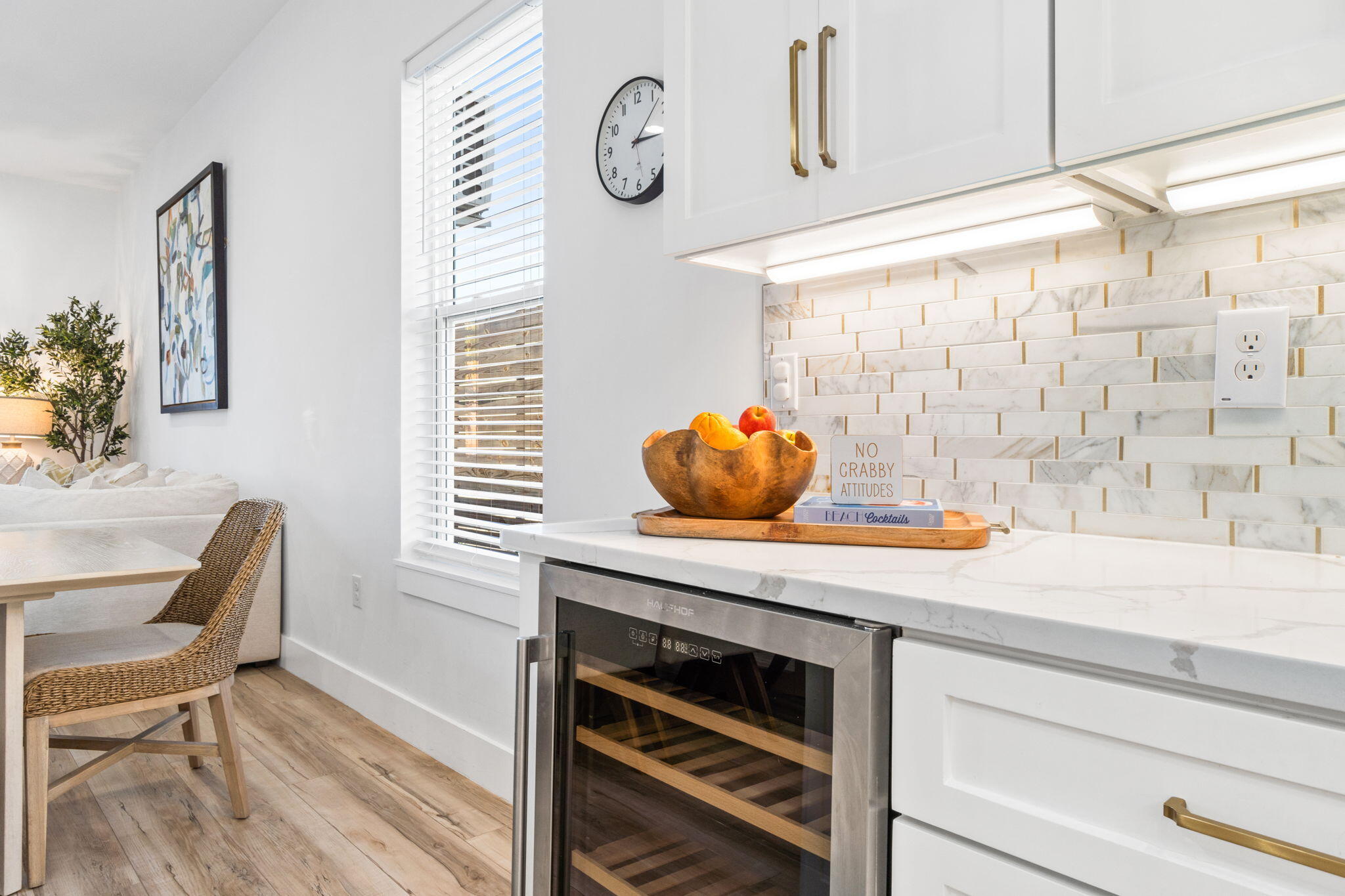 Bright white kitchen with marble-look backsplash, brass hardware, and a built-in wine cooler beside the dining area.