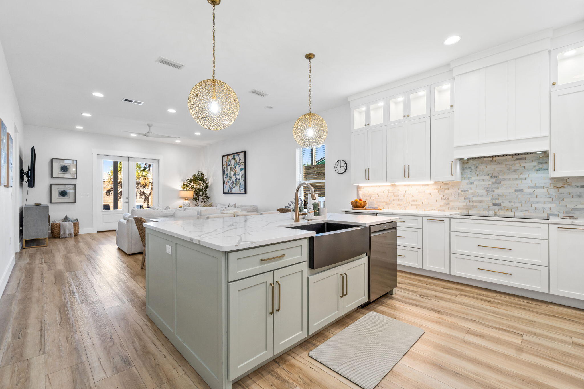 Bright white kitchen with a large marble-look island, brass pendants, and an adjoining living area.
