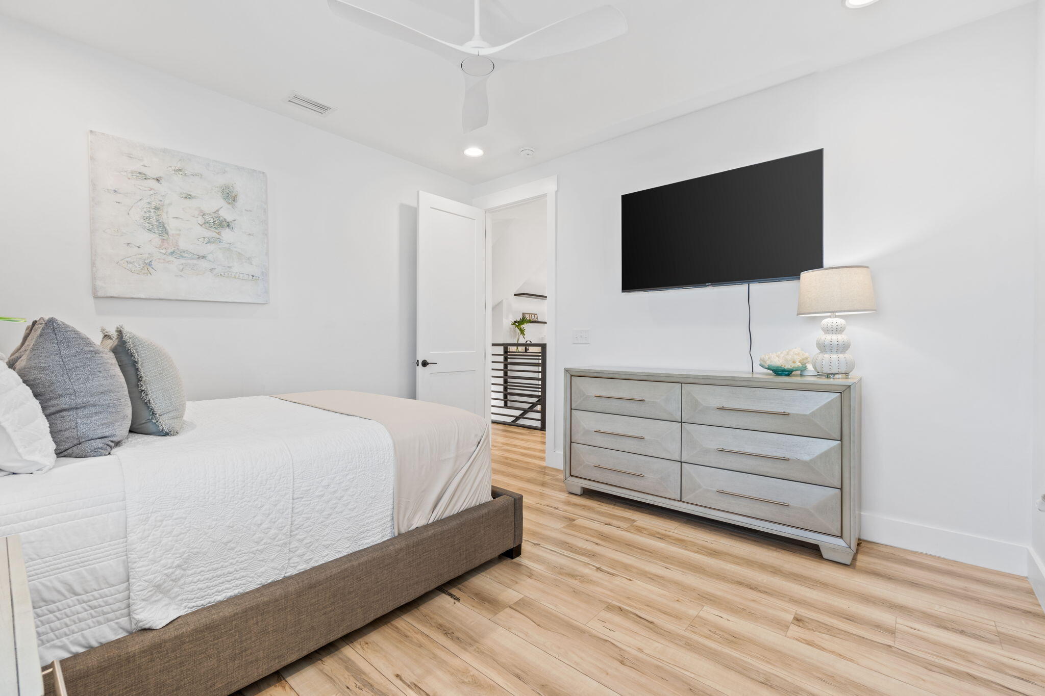 Bedroom with a white quilted bed, wall-mounted television, and light wood-look flooring.