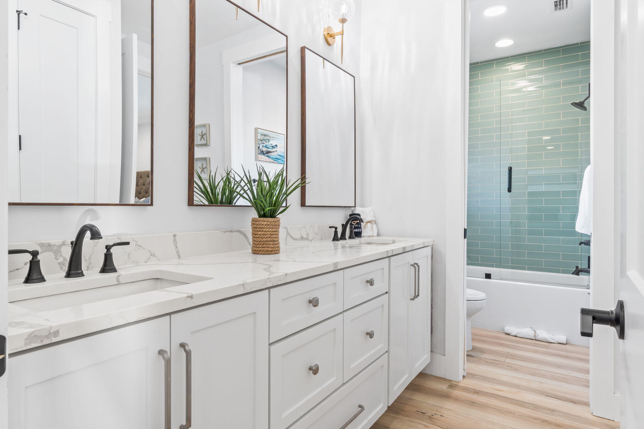 Bathroom with a white double vanity, marble counters, wood-framed mirrors, and teal-tiled shower.