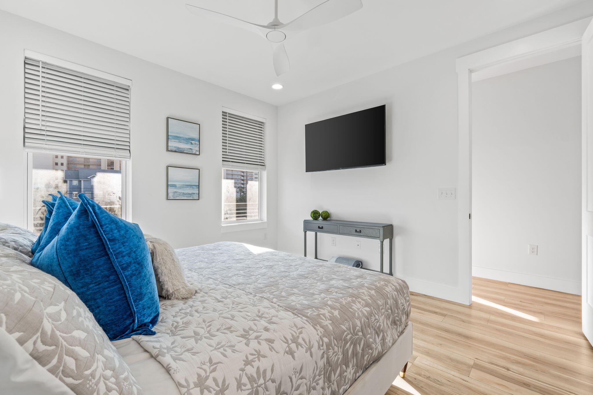 Bright bedroom with blue accent pillows, a patterned bedspread, and a wall-mounted television.