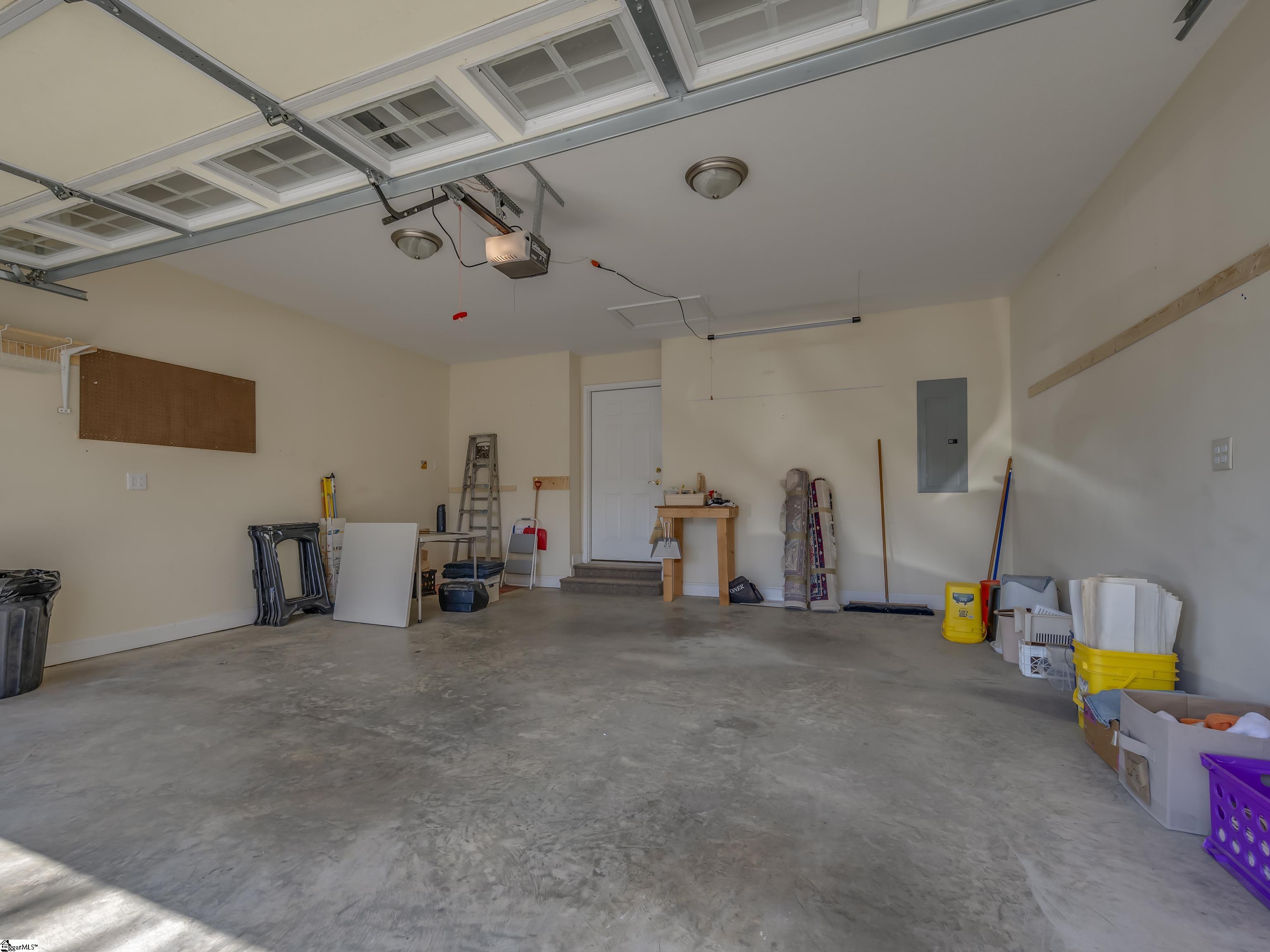Garage with a raised door, concrete floor, and storage items along the walls.