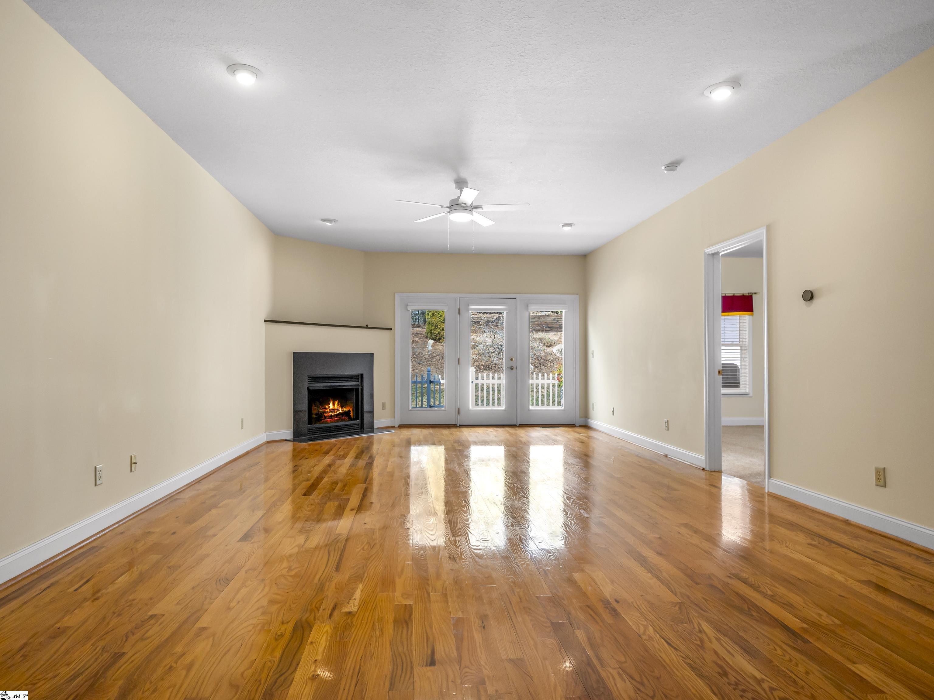 Empty living room with polished hardwood floors, a lit fireplace, and French doors.