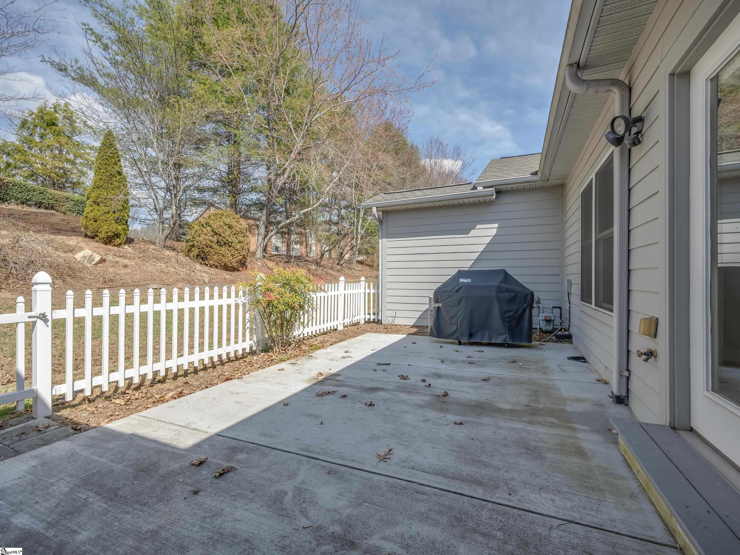 Concrete patio with a covered grill beside a white picket fence and sloping yard.