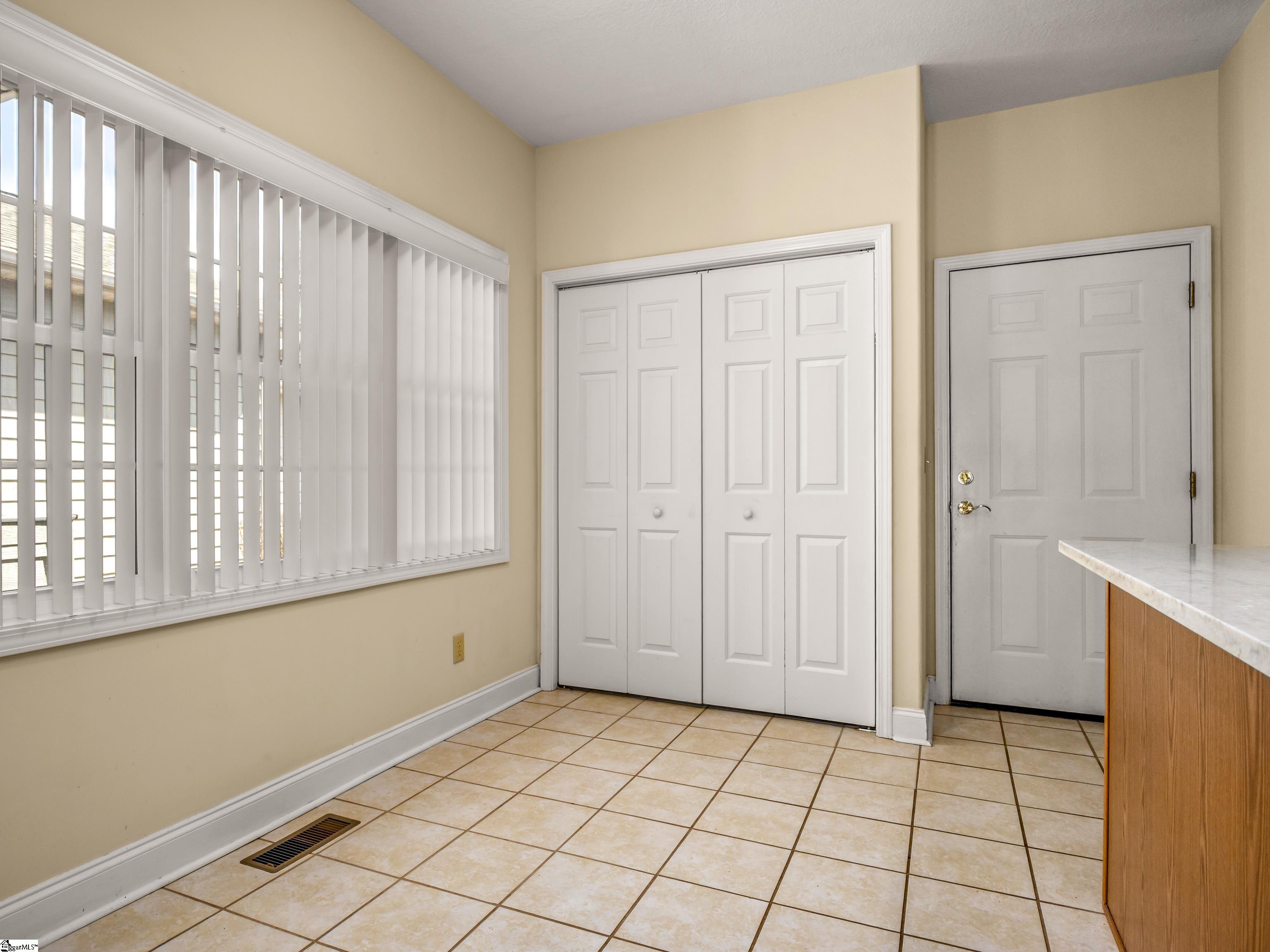Tiled room with vertical blinds, white closet doors, and an exterior entry door.