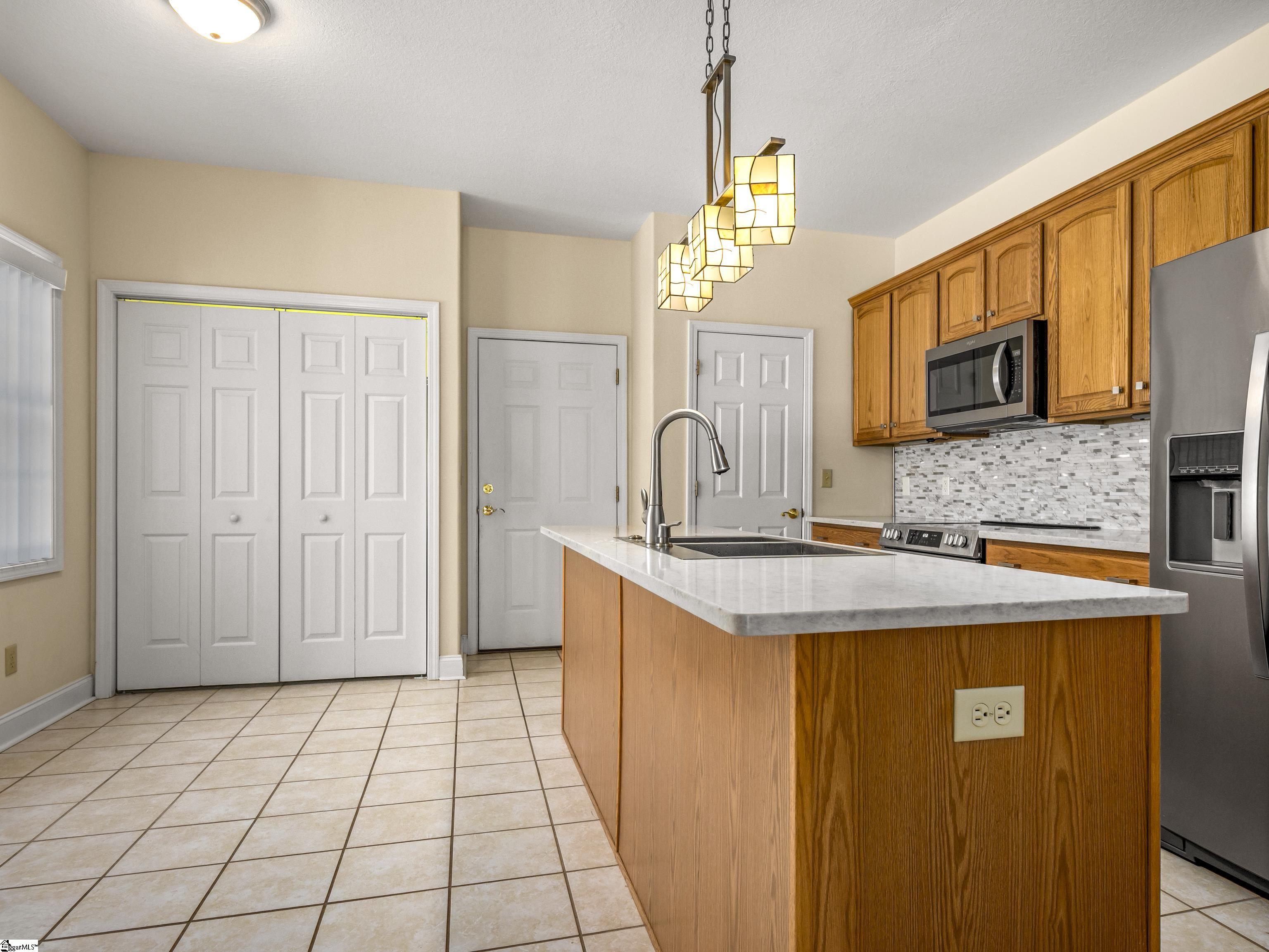 Kitchen with a large wood-paneled island, white countertop, honey-colored cabinets, and stainless steel appliances.