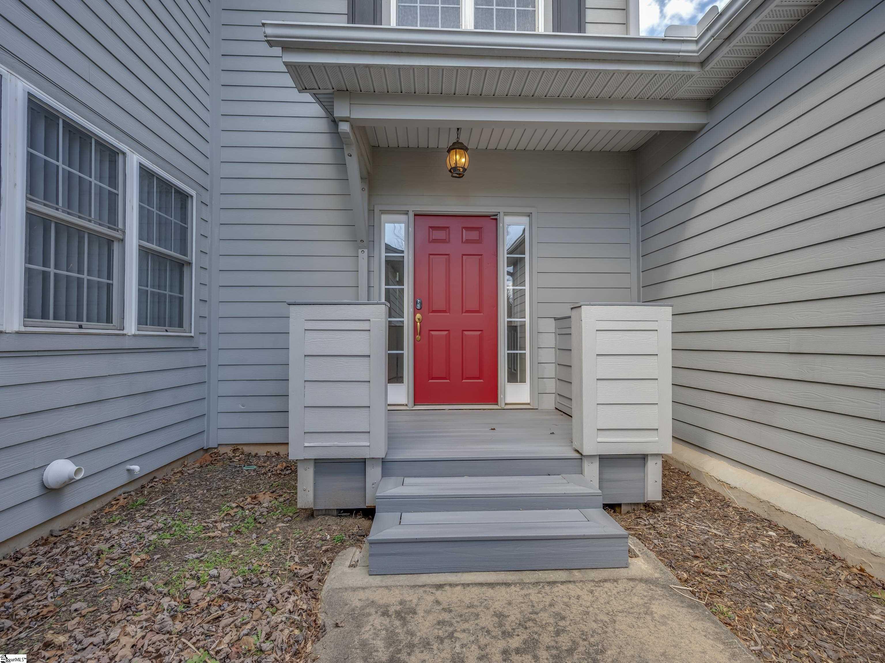 Gray house entry with a bright red front door, covered porch, and steps.