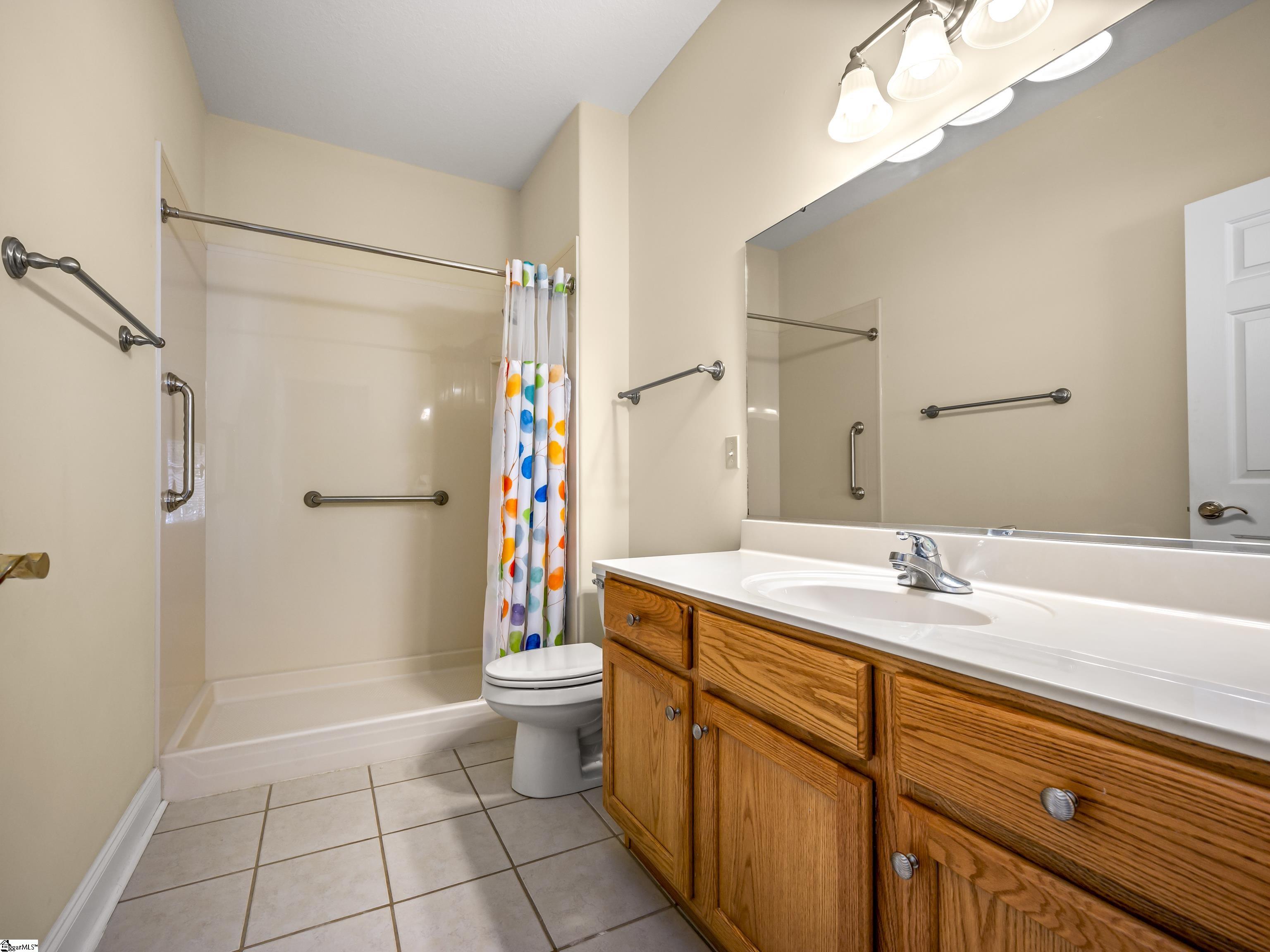 Bathroom with a polka-dot shower curtain, oak vanity, and grab bars beside the tub.