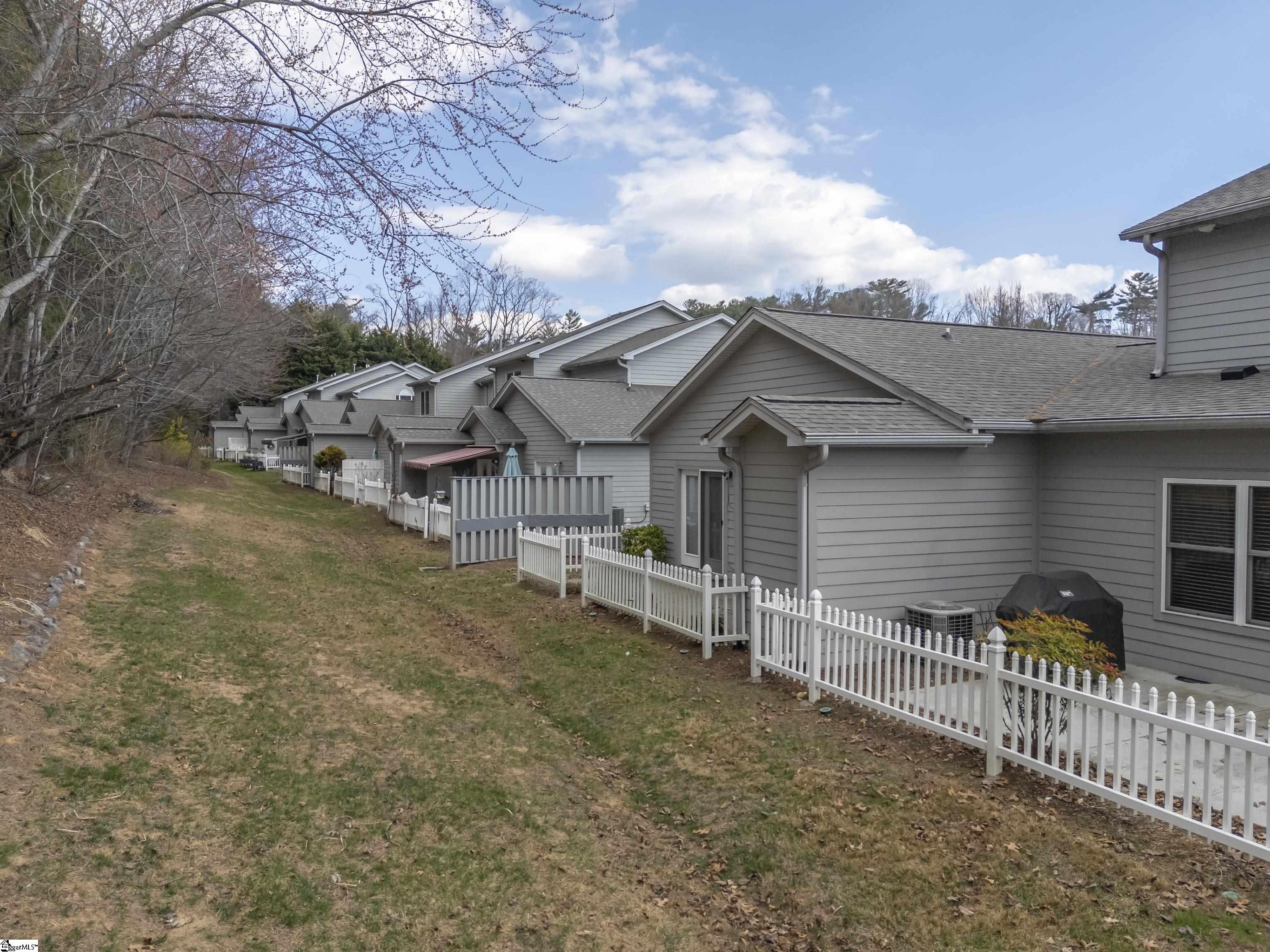 Gray attached homes with white fences line a grassy side yard.
