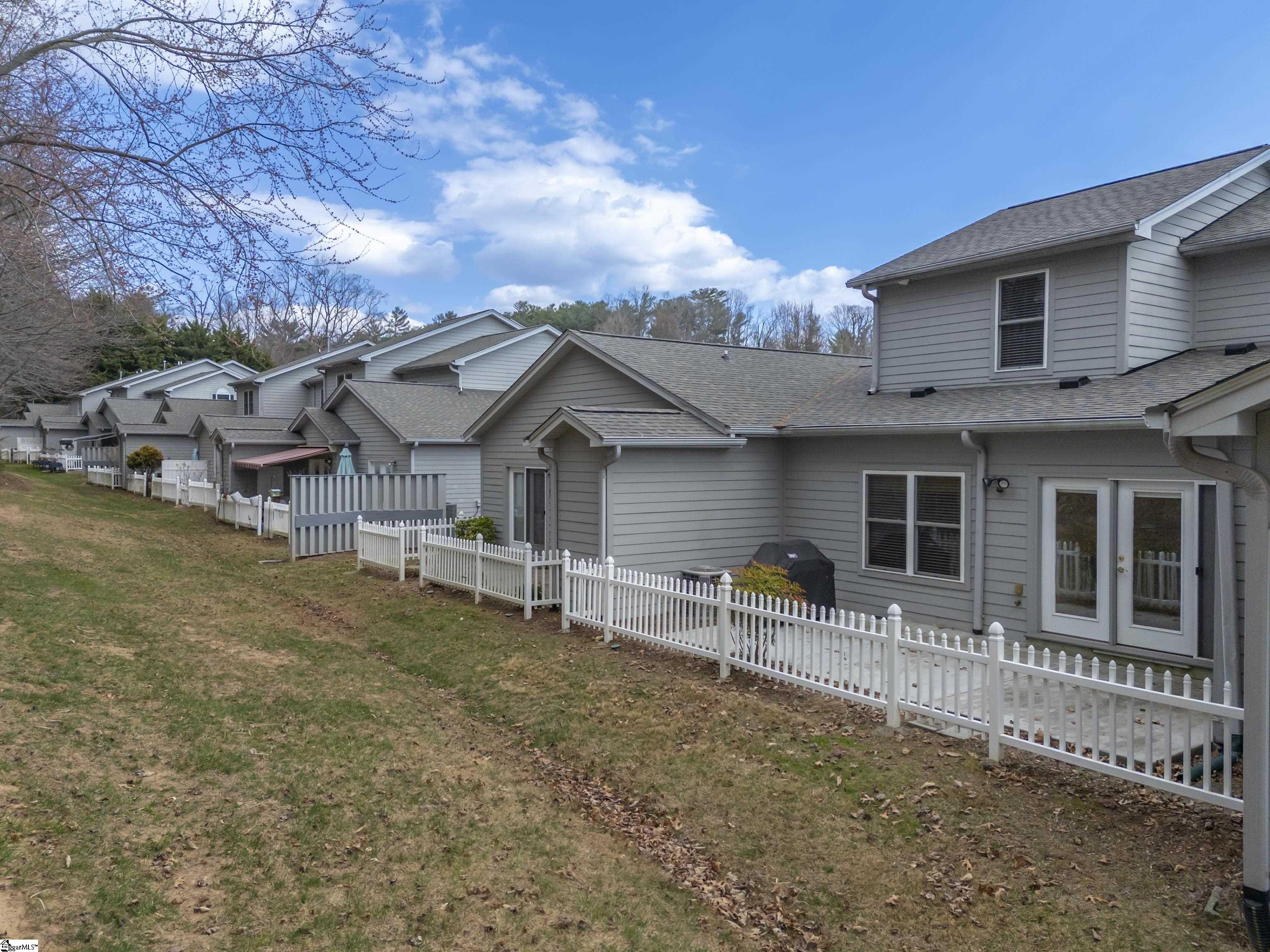 Gray-sided attached homes with fenced patios along a sloping lawn.