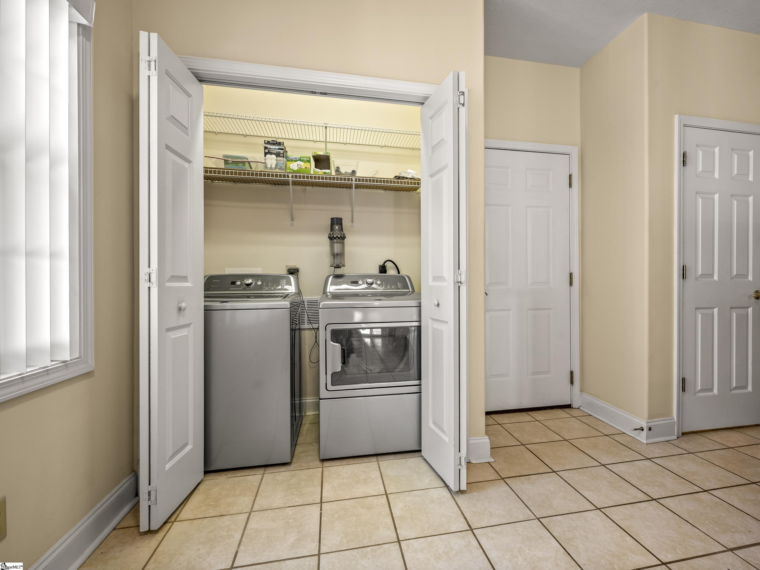 Laundry room with washer and dryer behind open doors and wire shelves above.
