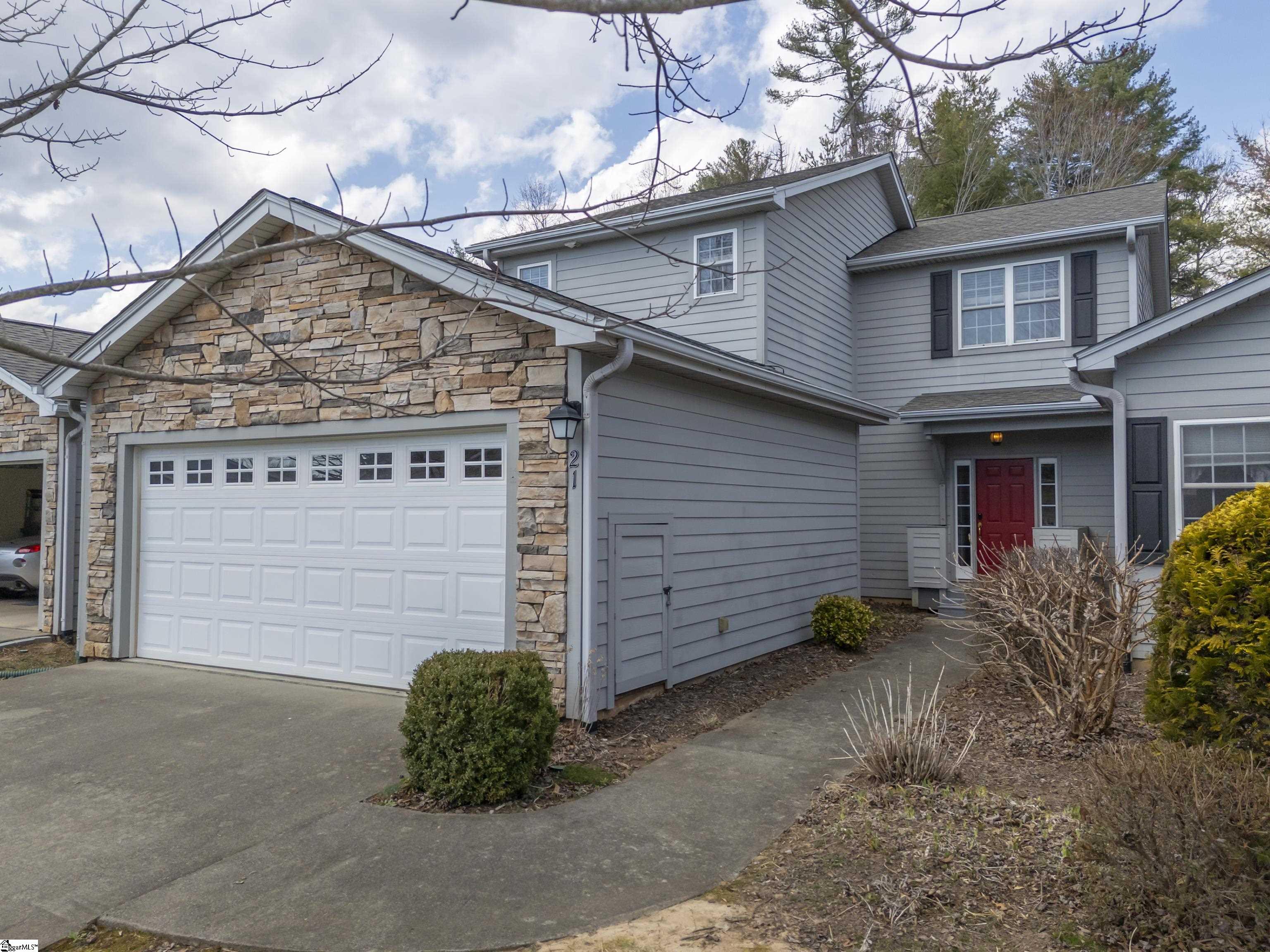 Two-story gray house with a stone-front garage, red entry door, and concrete driveway.