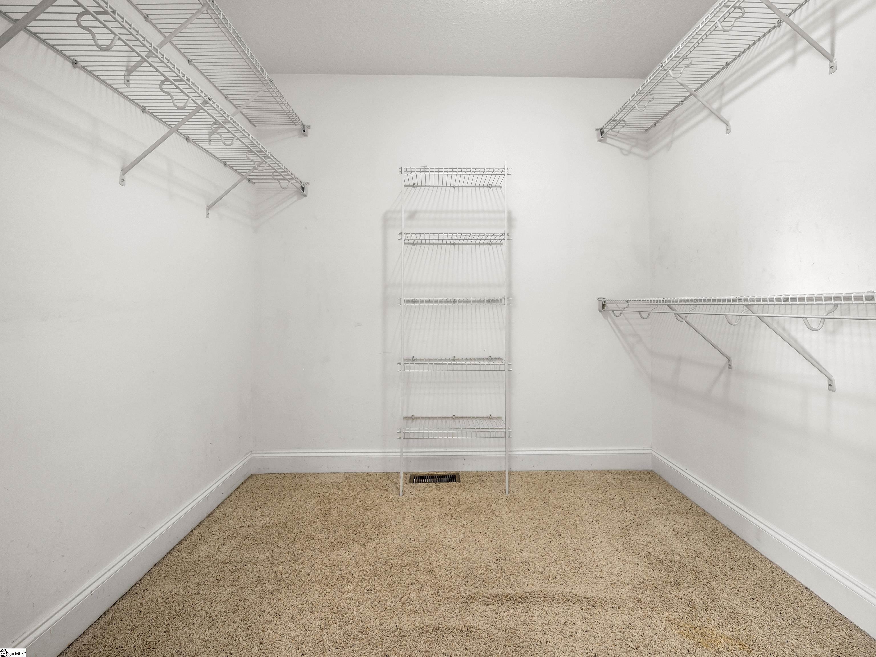 Empty walk-in closet with beige carpet and white wire shelving on three sides.