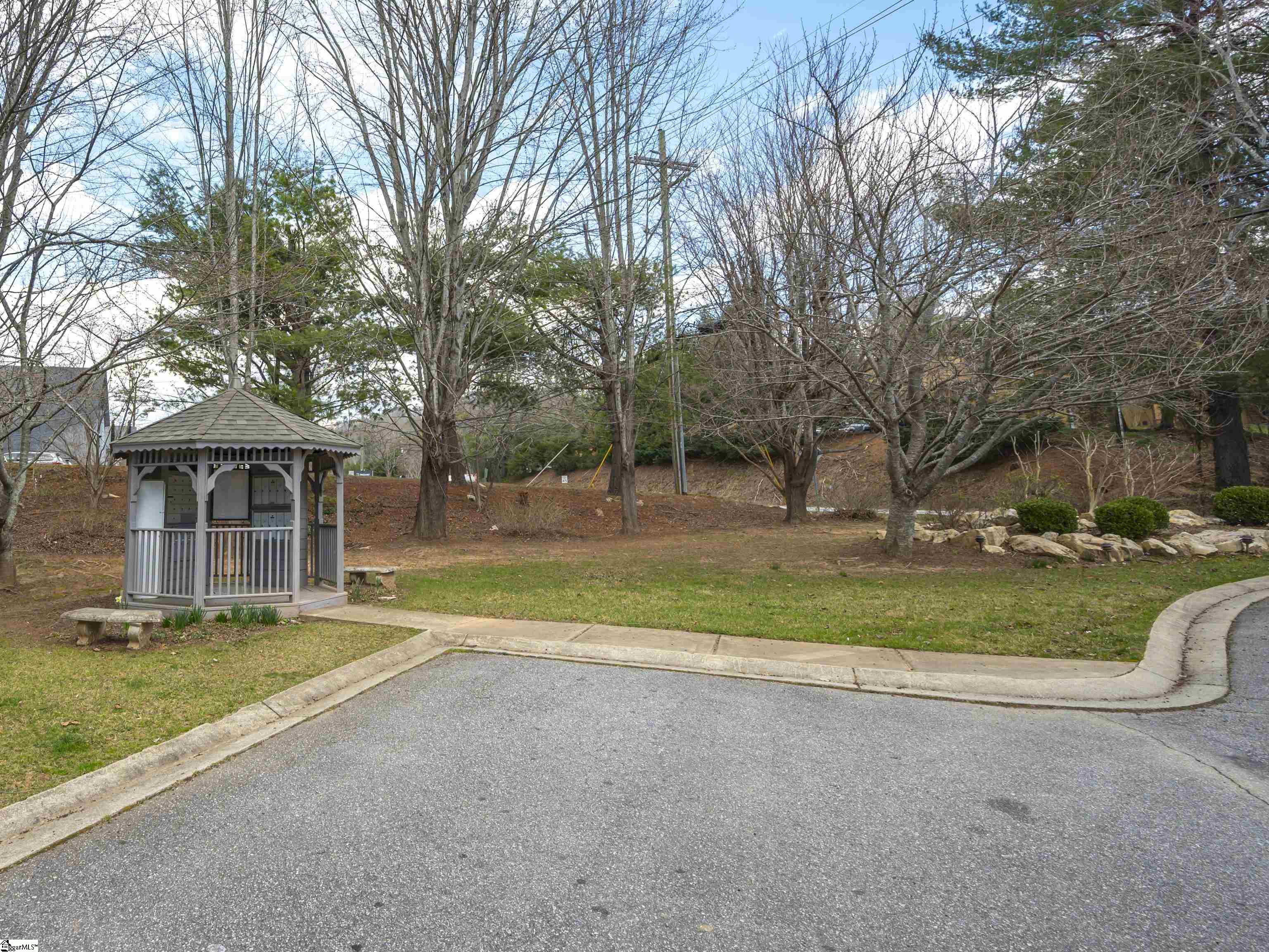Community gazebo beside a paved drive, surrounded by leafless trees and landscaped grounds.