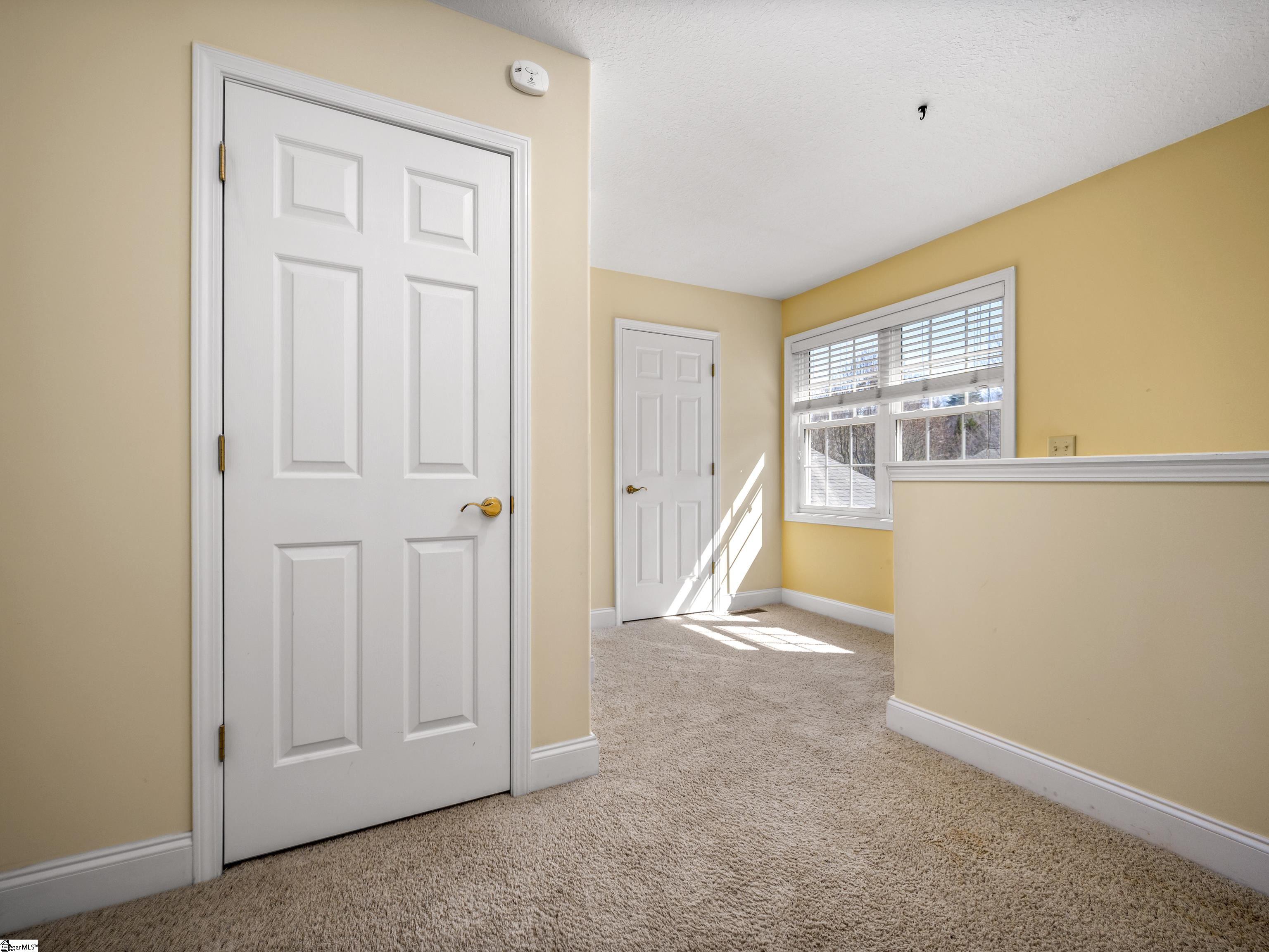 Empty yellow room with beige carpet, two white doors, and a sunlit window with blinds.