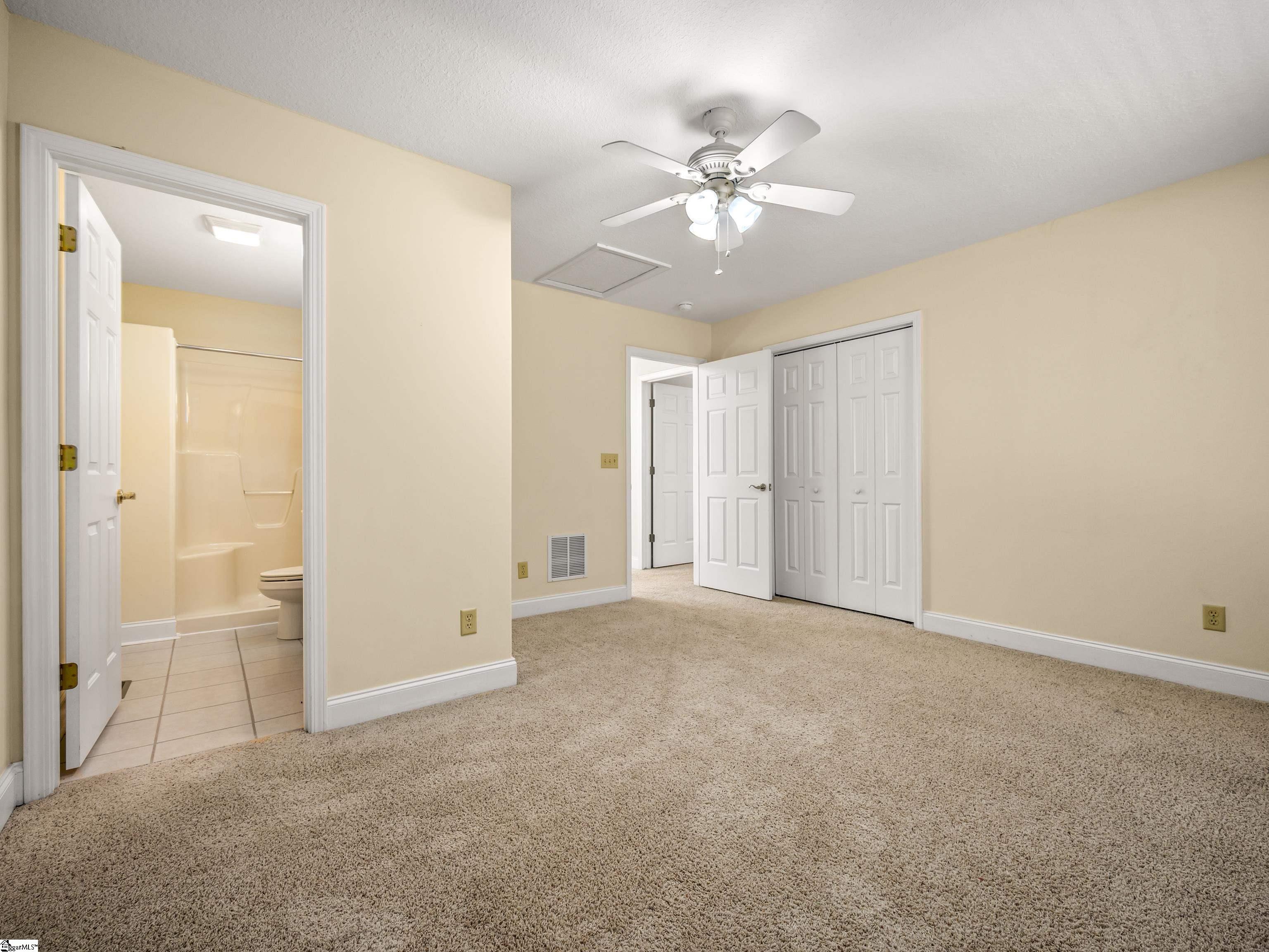 Empty carpeted bedroom with a ceiling fan, double closets, and an adjoining bathroom.