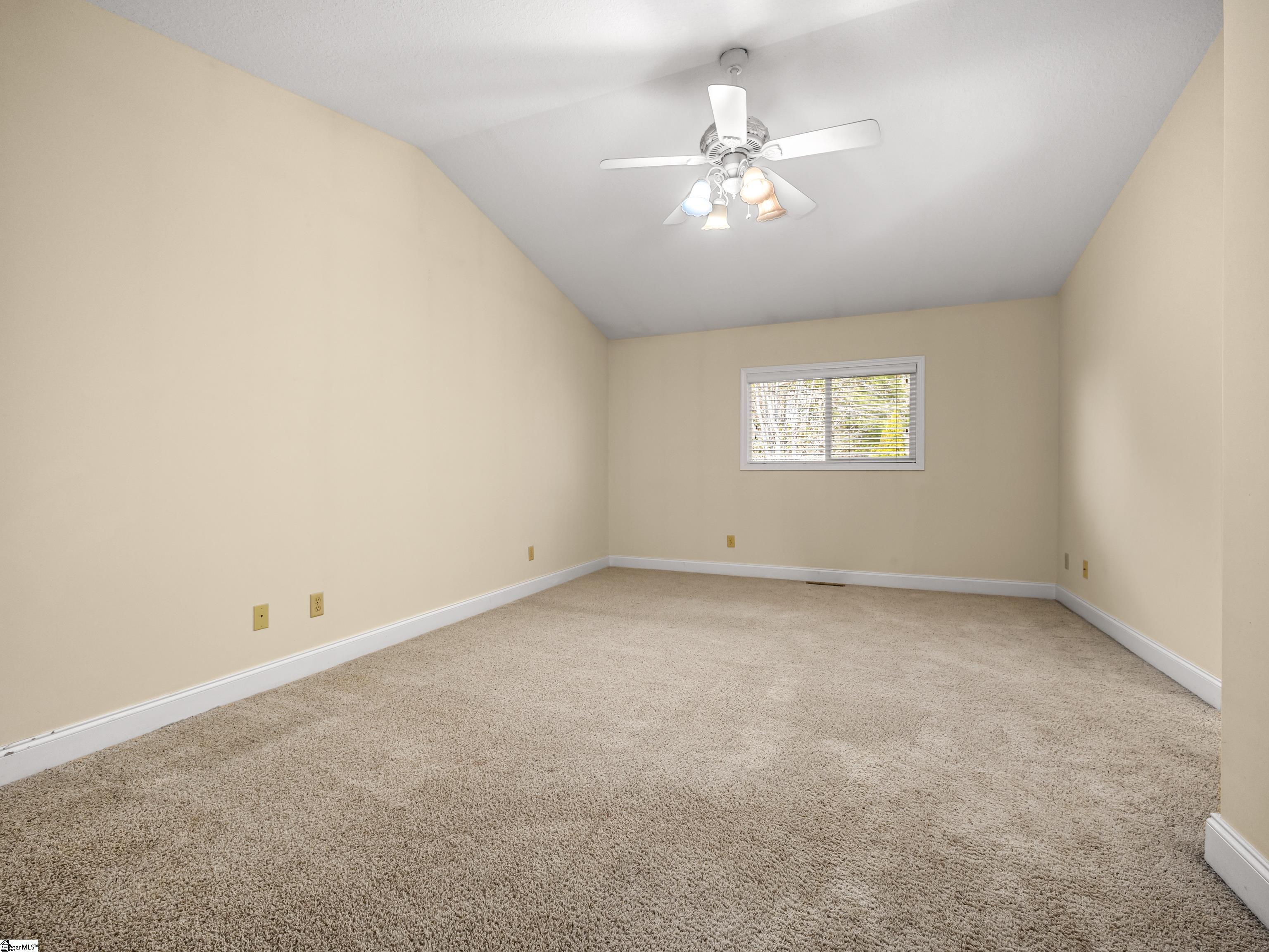 Empty carpeted room with beige walls, a ceiling fan, and a window with blinds.