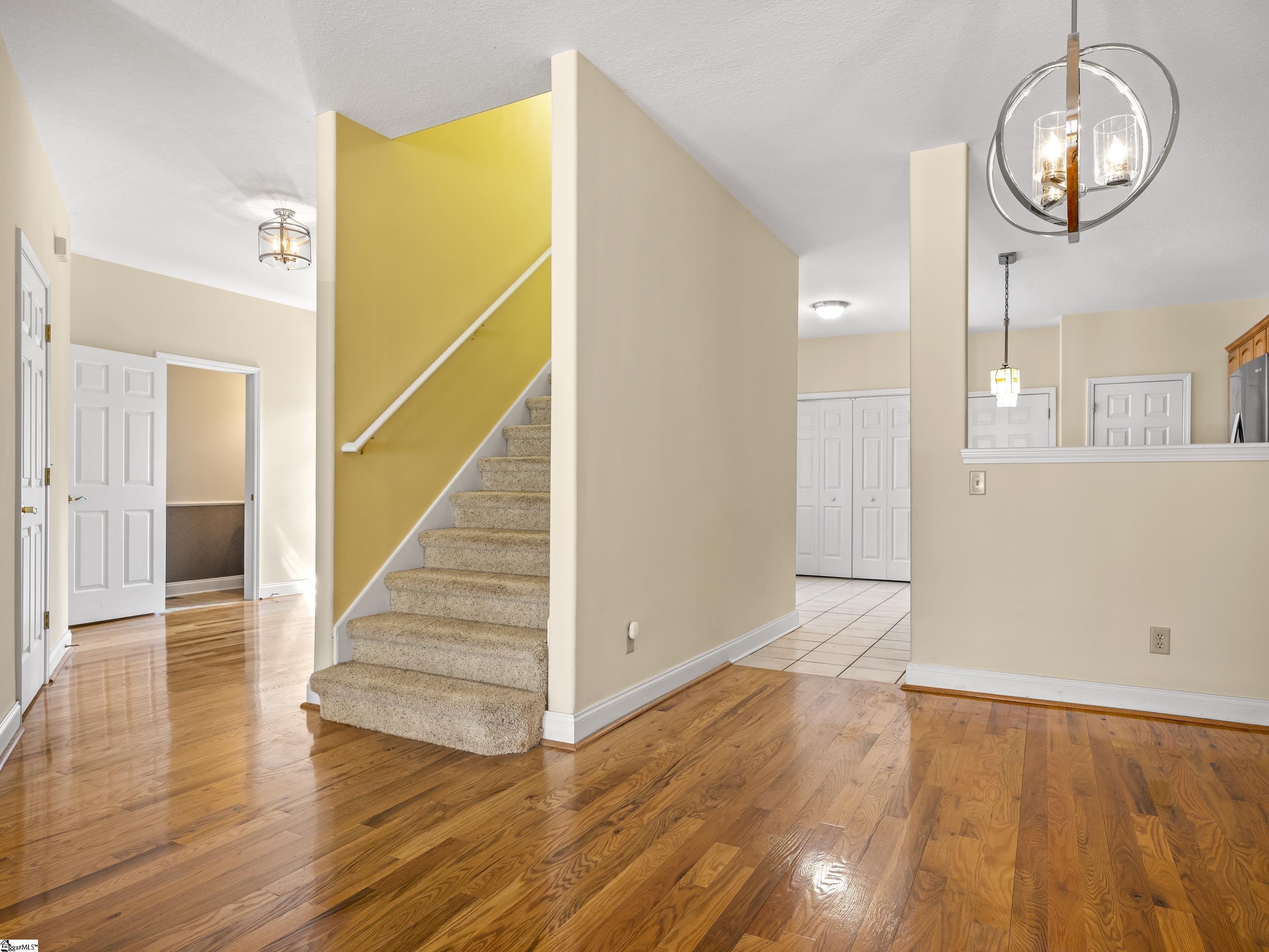 Entry hall with polished hardwood floors and a carpeted staircase against a mustard-yellow wall.