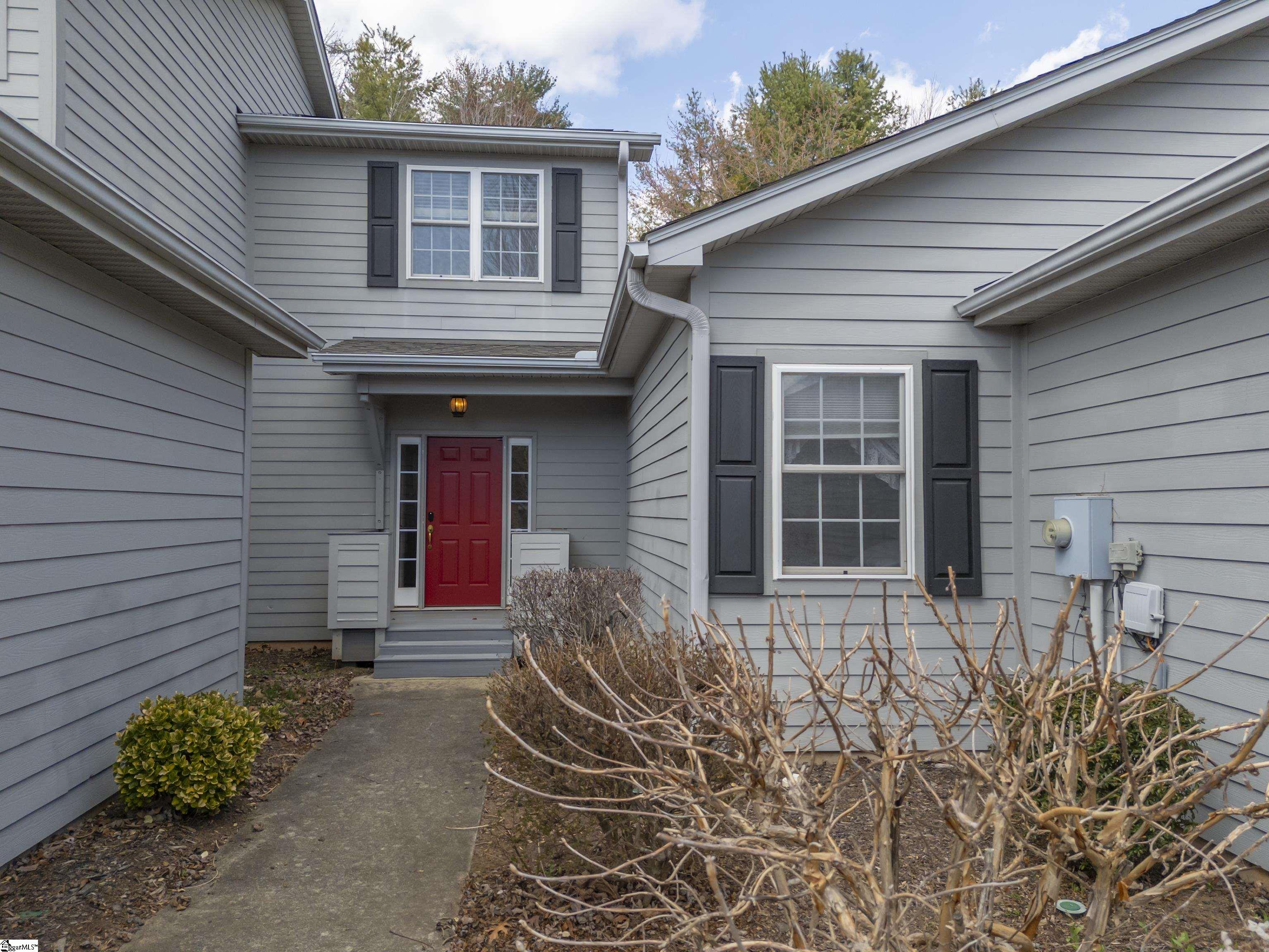 Gray two-story house with black shutters, a red front door, and a walkway through dormant shrubs.