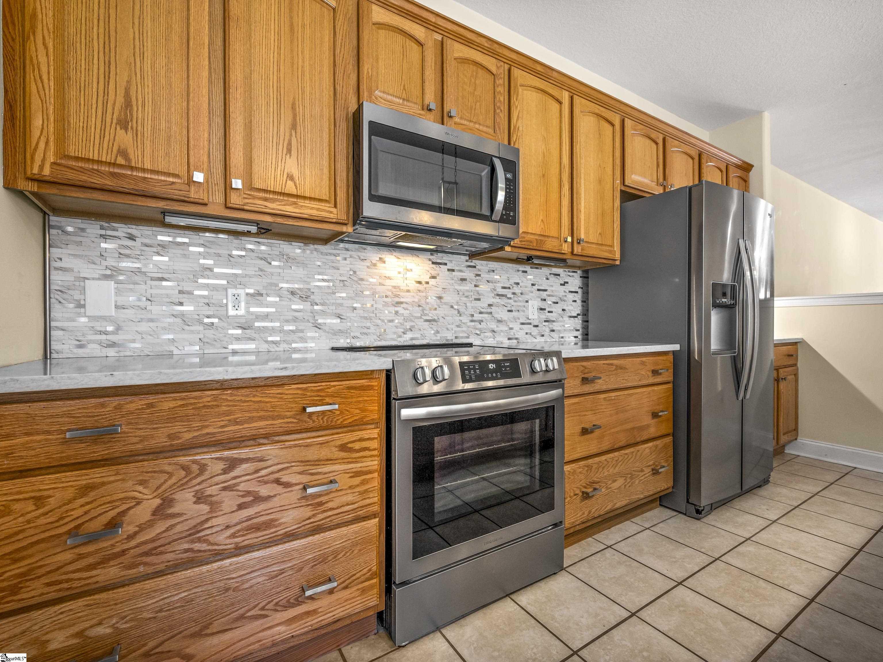 Kitchen with oak cabinetry, stainless-steel appliances, and a gray-and-white tile backsplash.