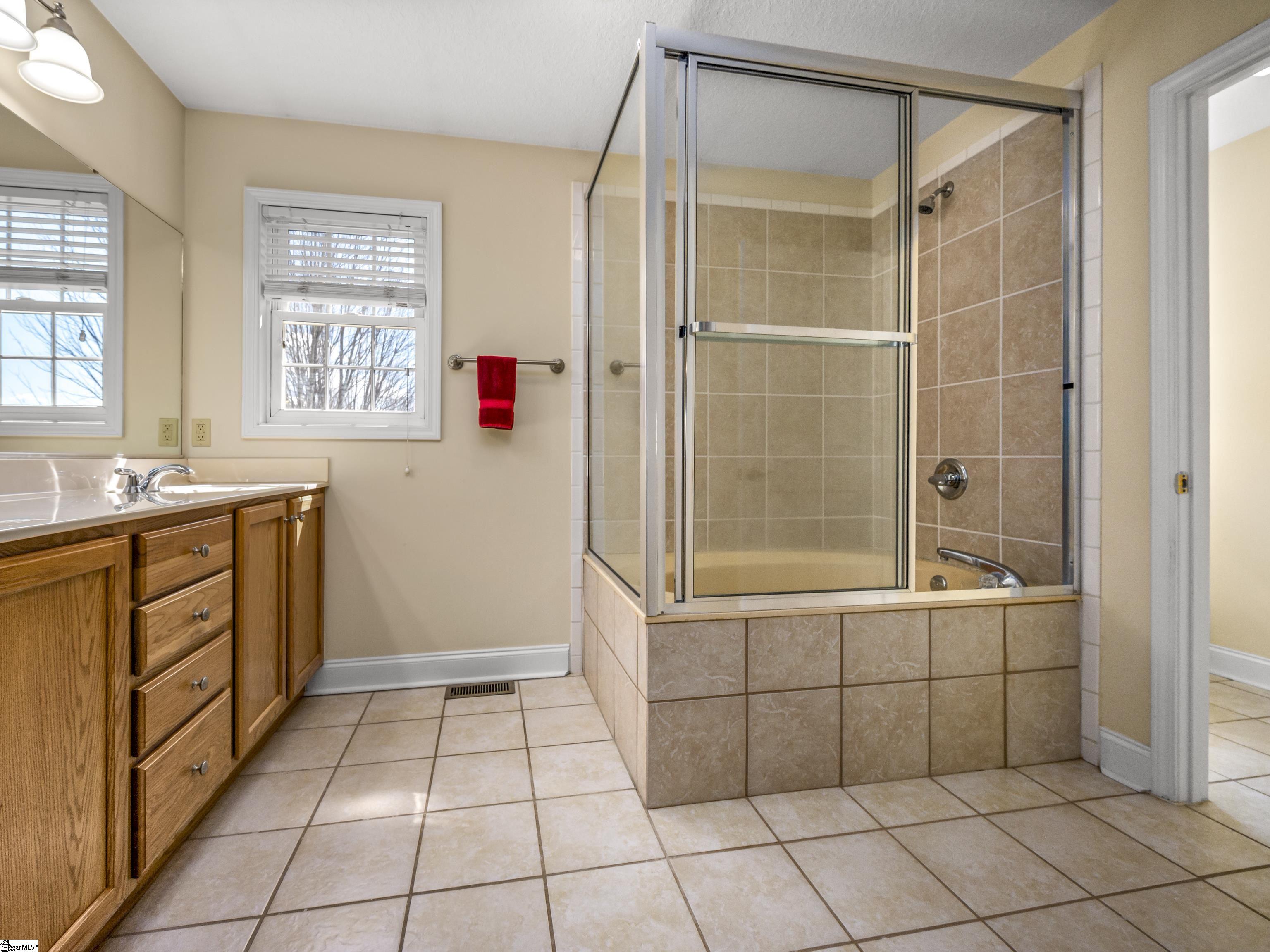 Bathroom with a glass-enclosed tiled tub, wood vanity, and red hand towel.