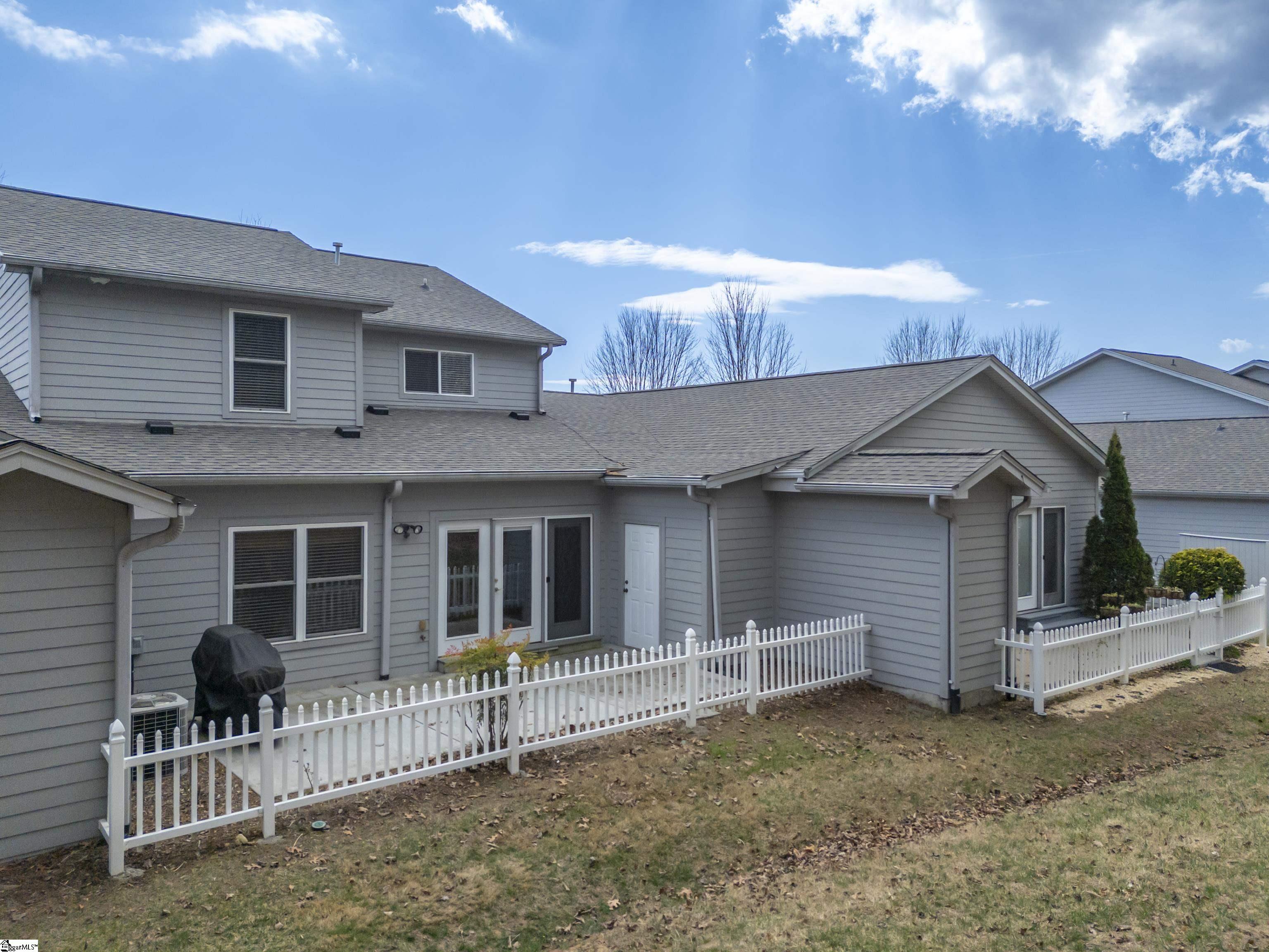 Rear of gray two-story home with a white picket fence enclosing the patio.