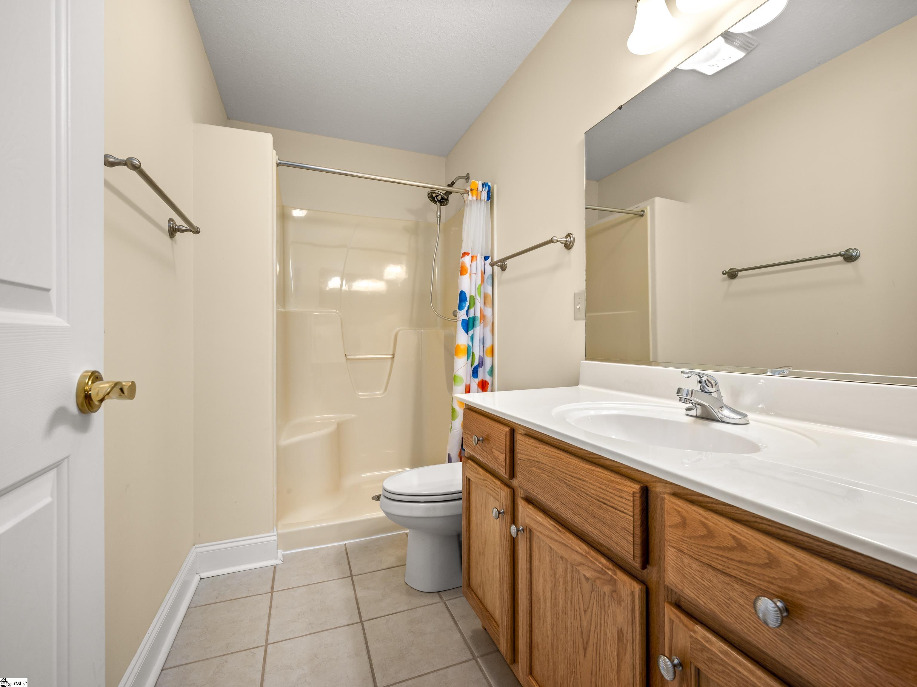 Bathroom with a colorful shower curtain, wood vanity, large mirror, and grab bars.