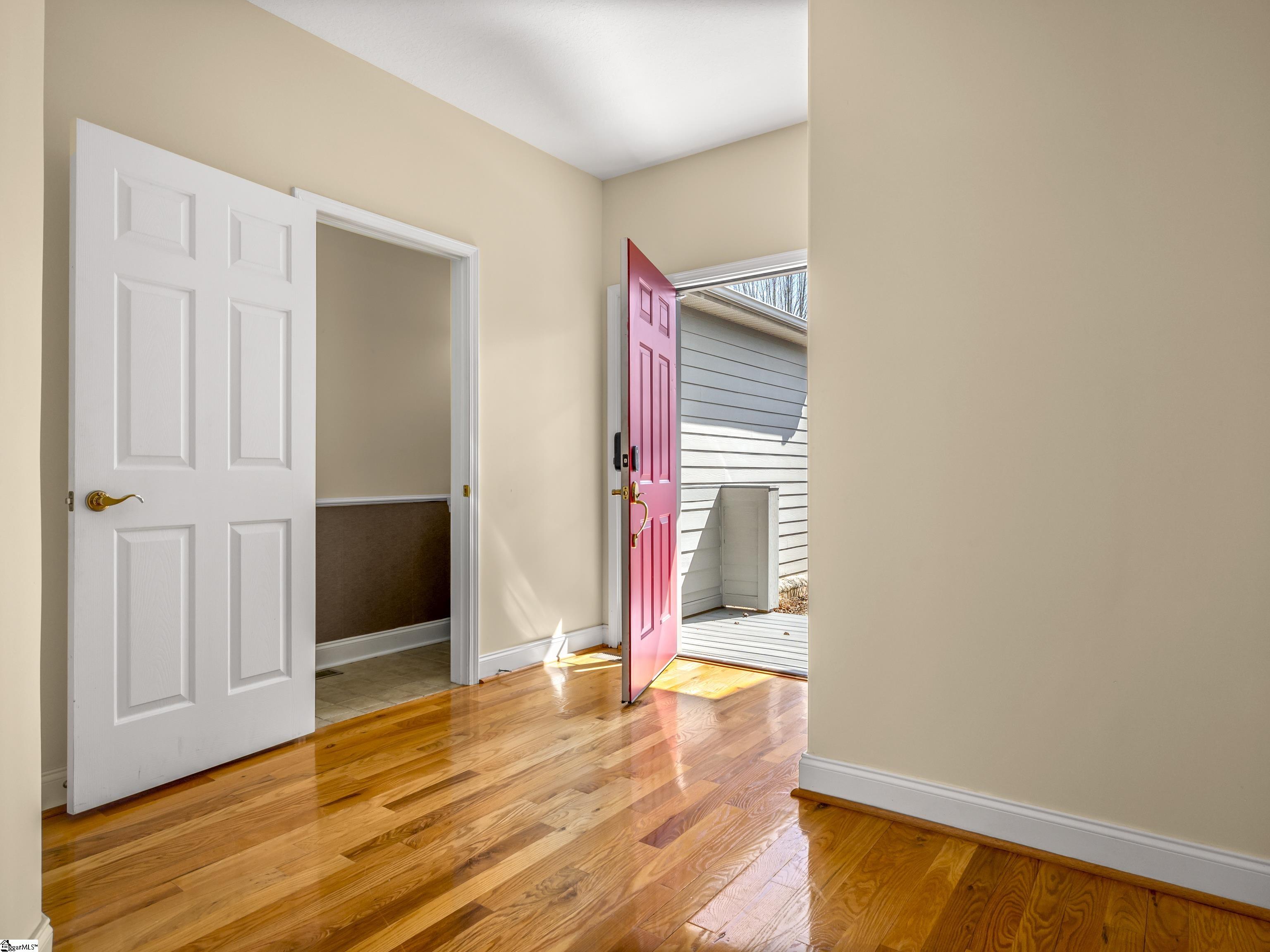 Entryway with glossy hardwood floors and an open pink-red front door.