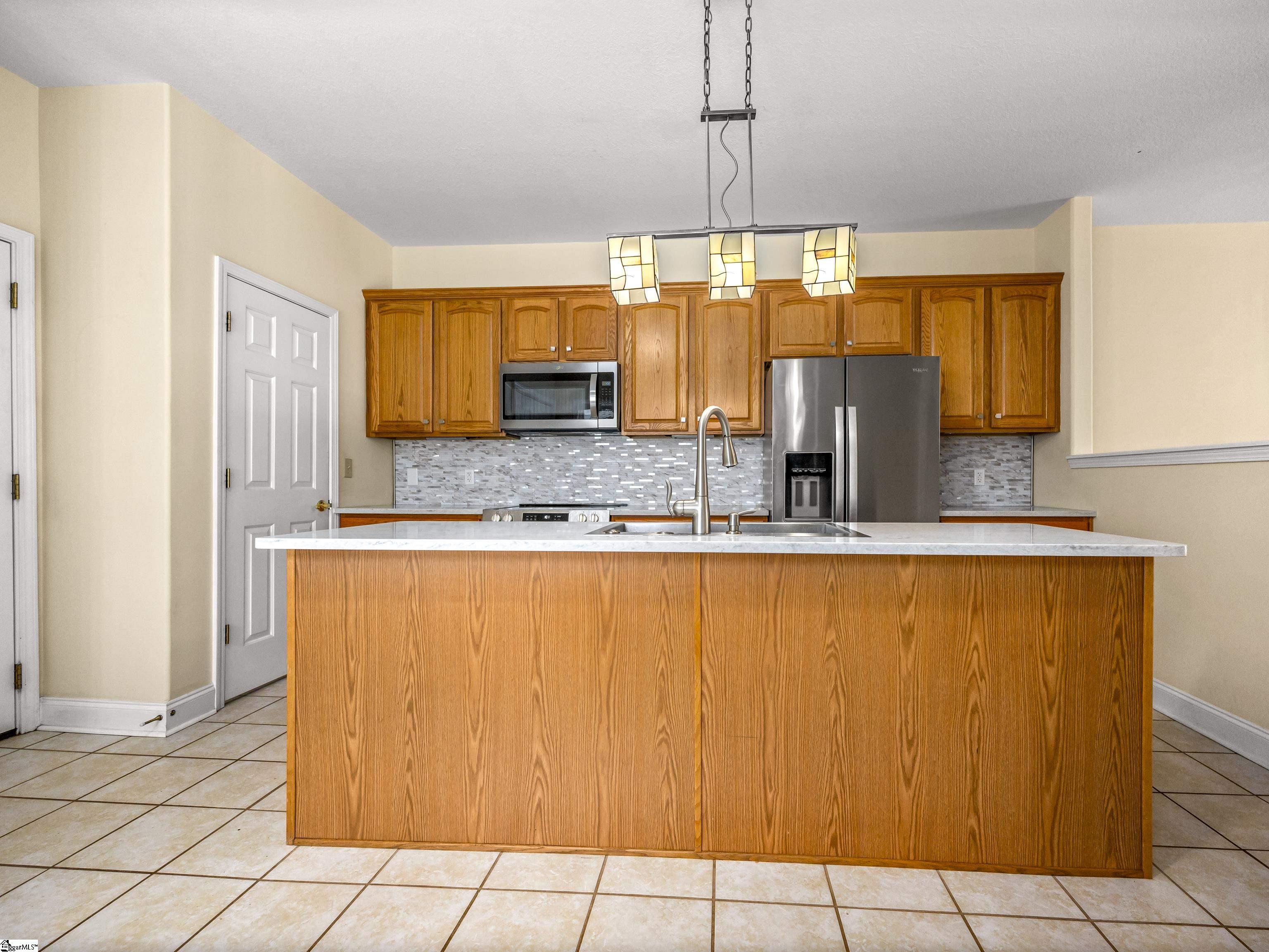 Kitchen with a large wood-paneled island, honey-toned cabinets, stainless appliances, and gray mosaic backsplash.