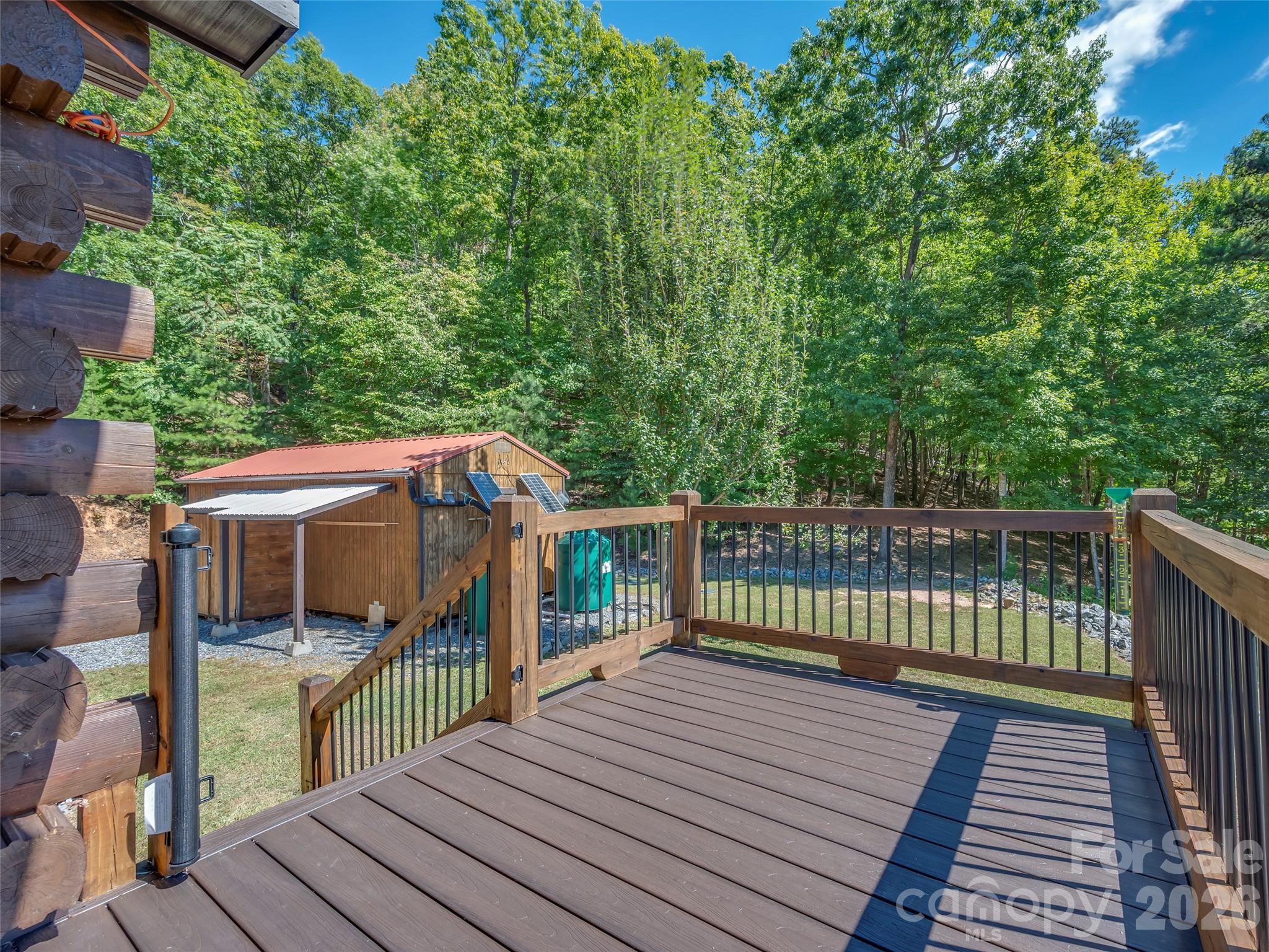 Wooden deck overlooking a solar-paneled outbuilding and dense green woods.