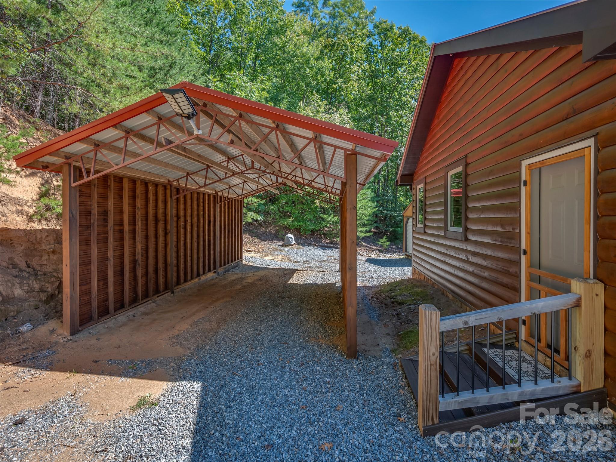 Wood-sided home beside a large timber carport with exposed trusses and a red metal roof.