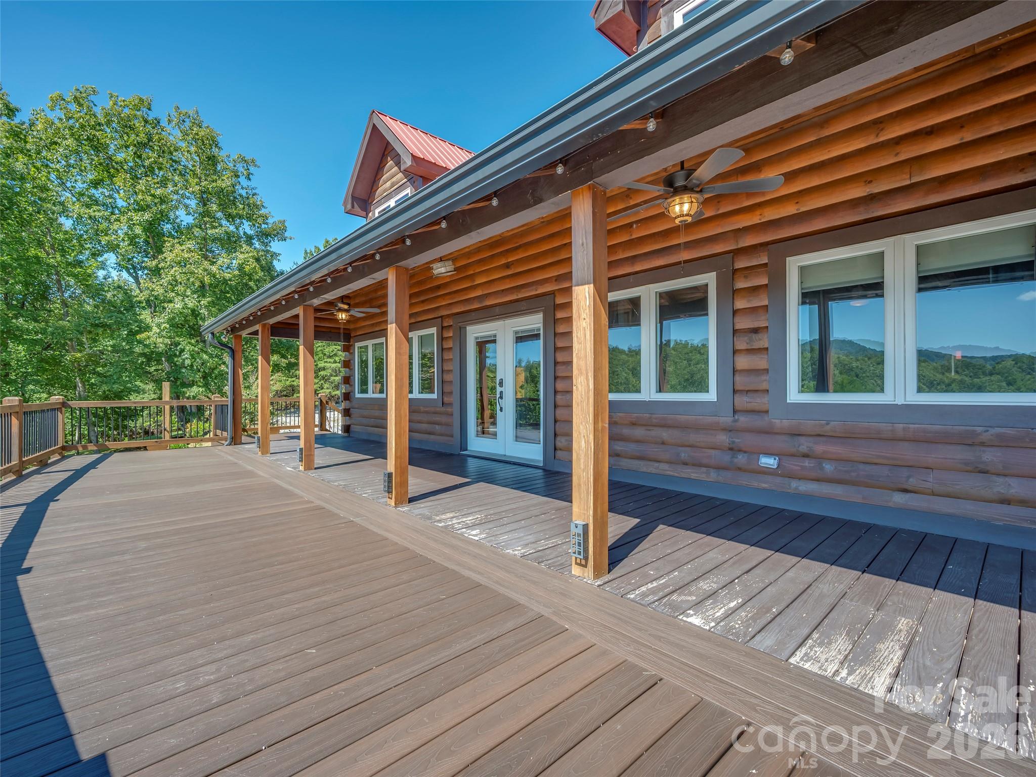 Log-sided home with a spacious covered deck, timber posts, ceiling fans, and wooded hills reflected in the windows.
