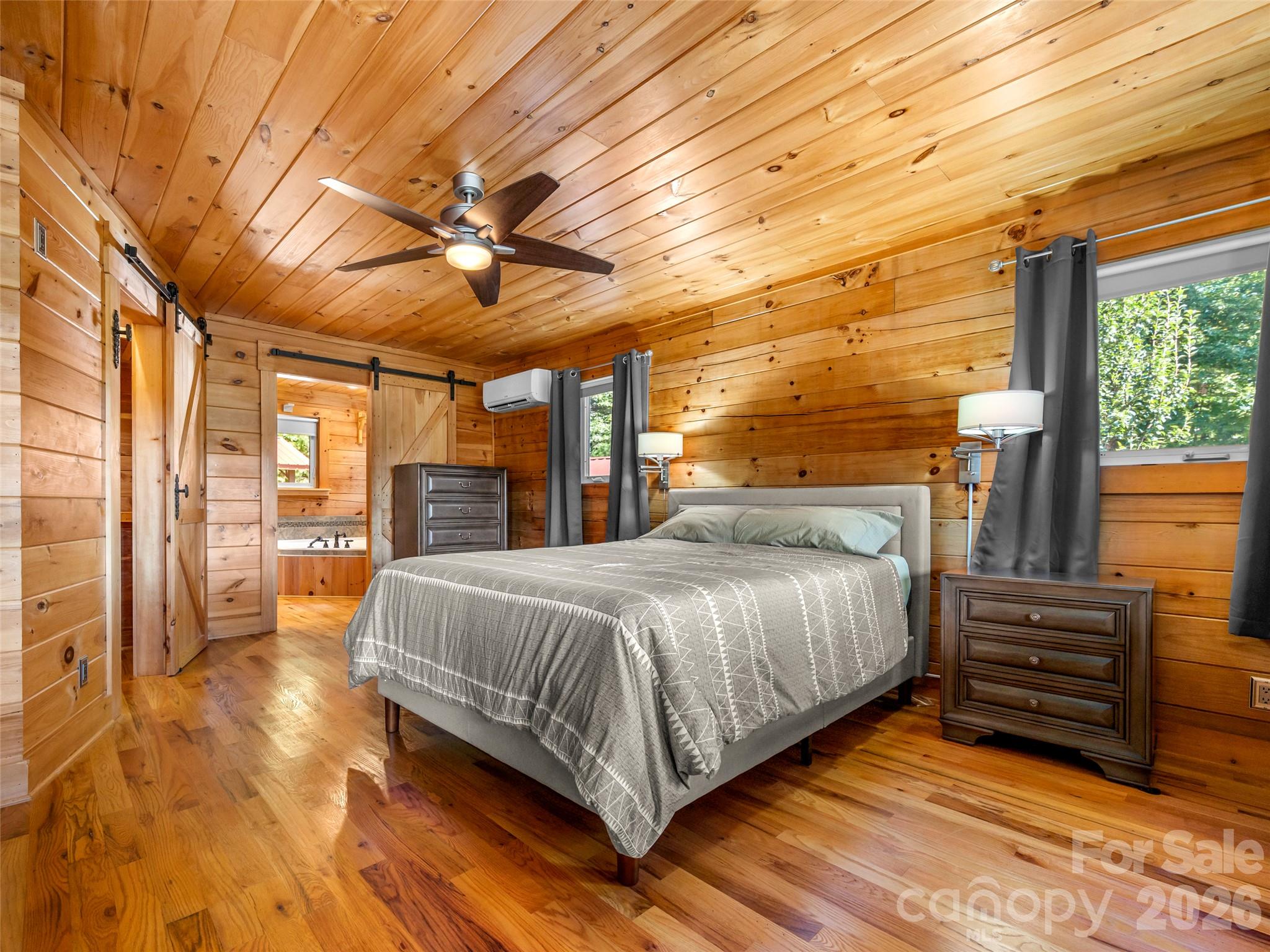 Bedroom with knotty-pine walls and ceiling, a gray bed, and sliding barn doors.