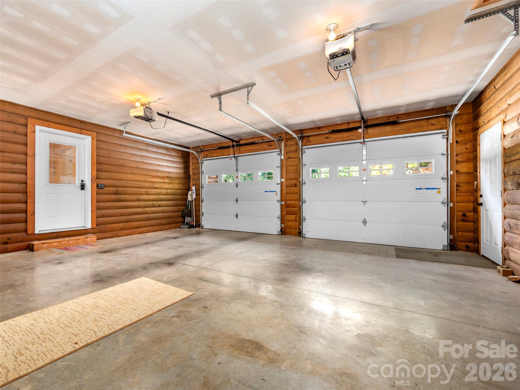 Empty garage with log-style wood walls, two overhead doors, and a concrete floor.