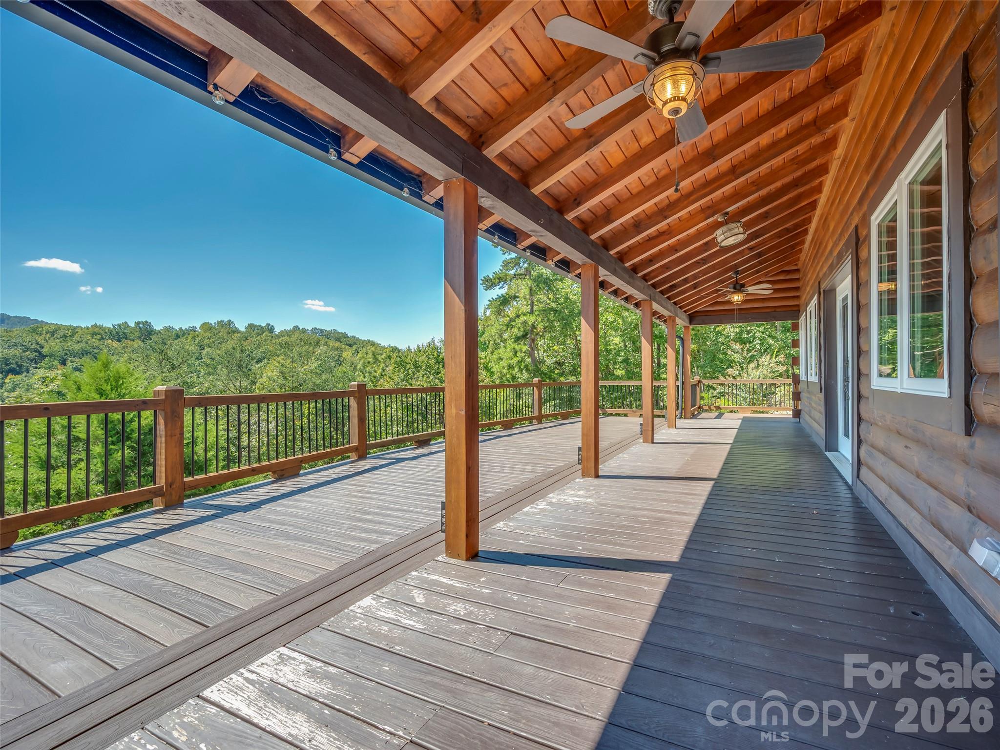 Covered wooden deck with timber posts and ceiling fans overlooking leafy hills.