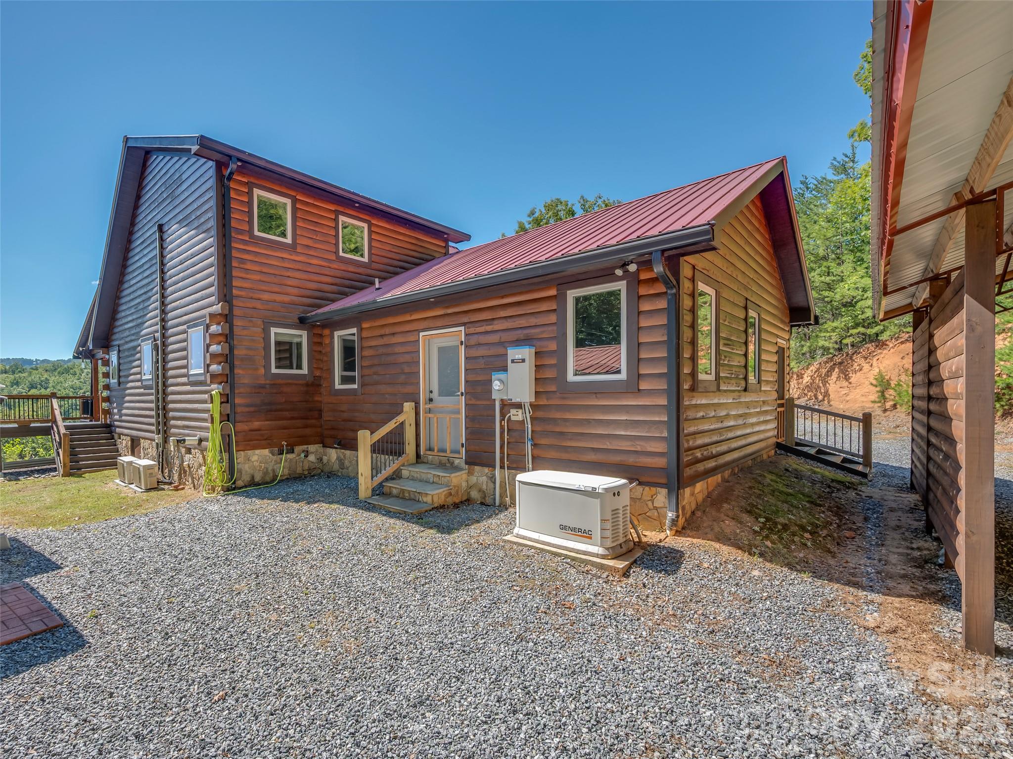 Log-sided home with red metal roof, gravel driveway, and standby generator