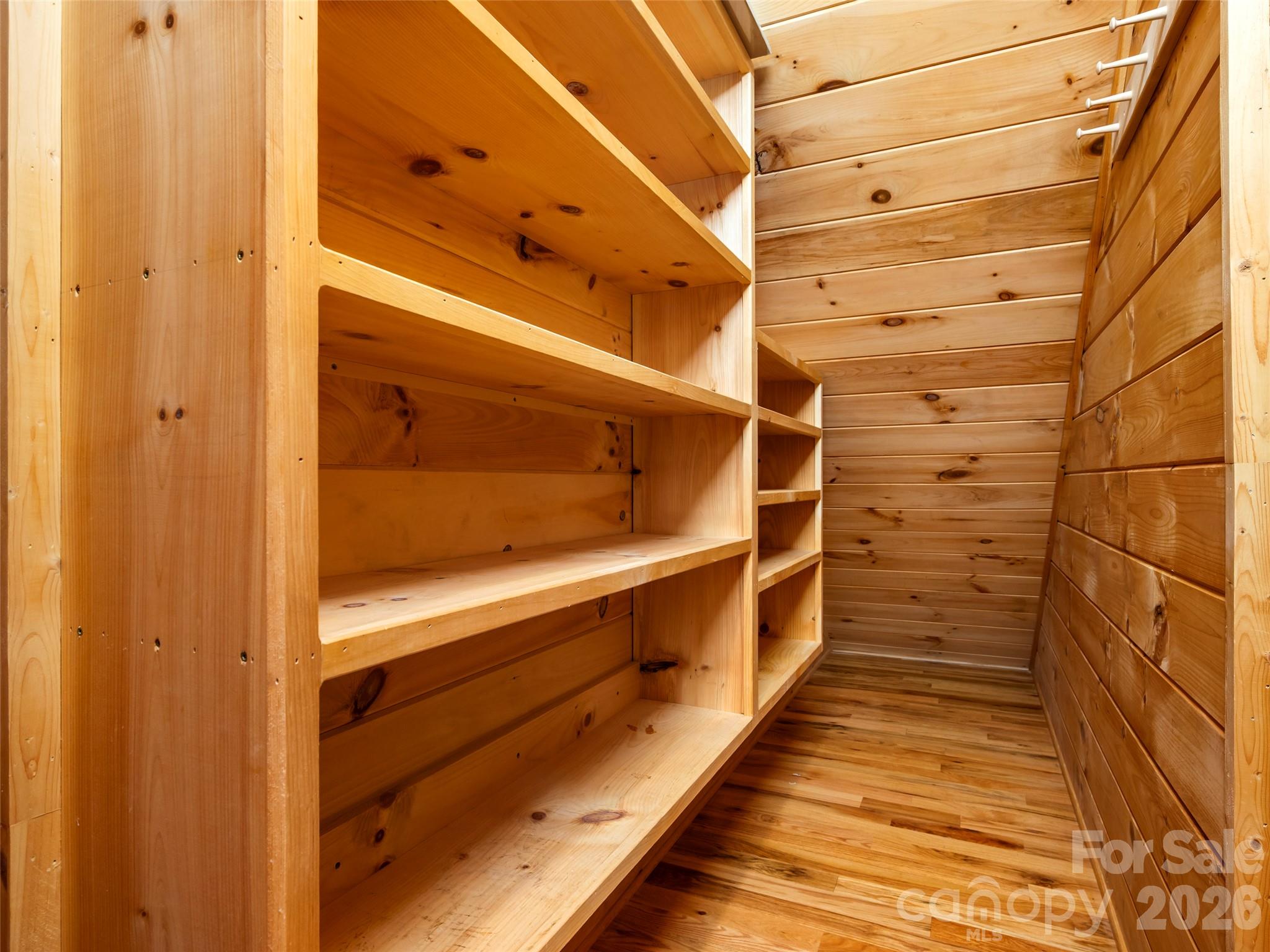 Walk-in closet with built-in wooden shelves and pine plank walls.