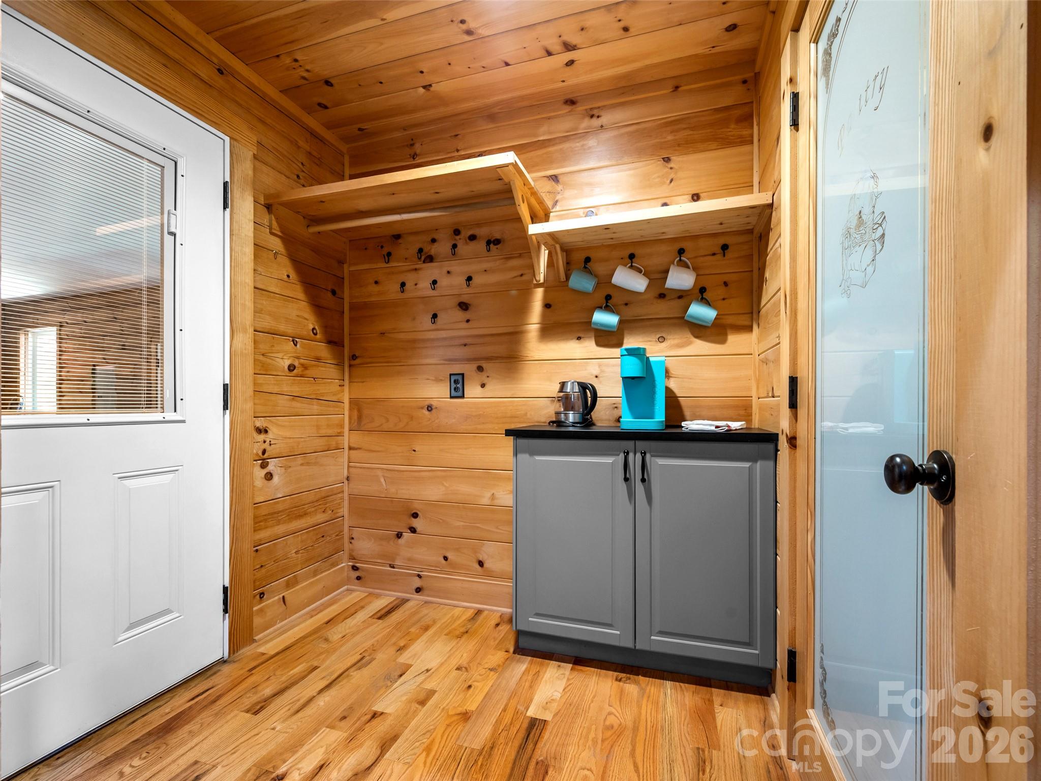 Wood-paneled coffee station with a gray cabinet, turquoise beverage machine, and hanging mugs.