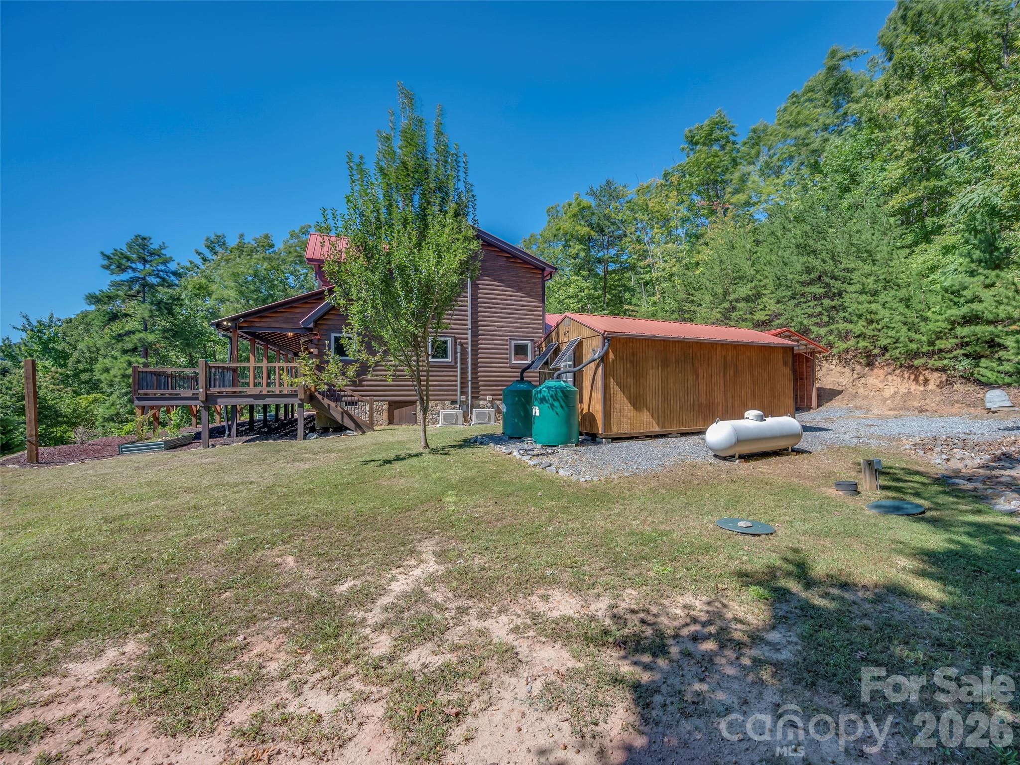 Log-sided cabin with a raised deck and separate wooden outbuilding in a wooded setting.