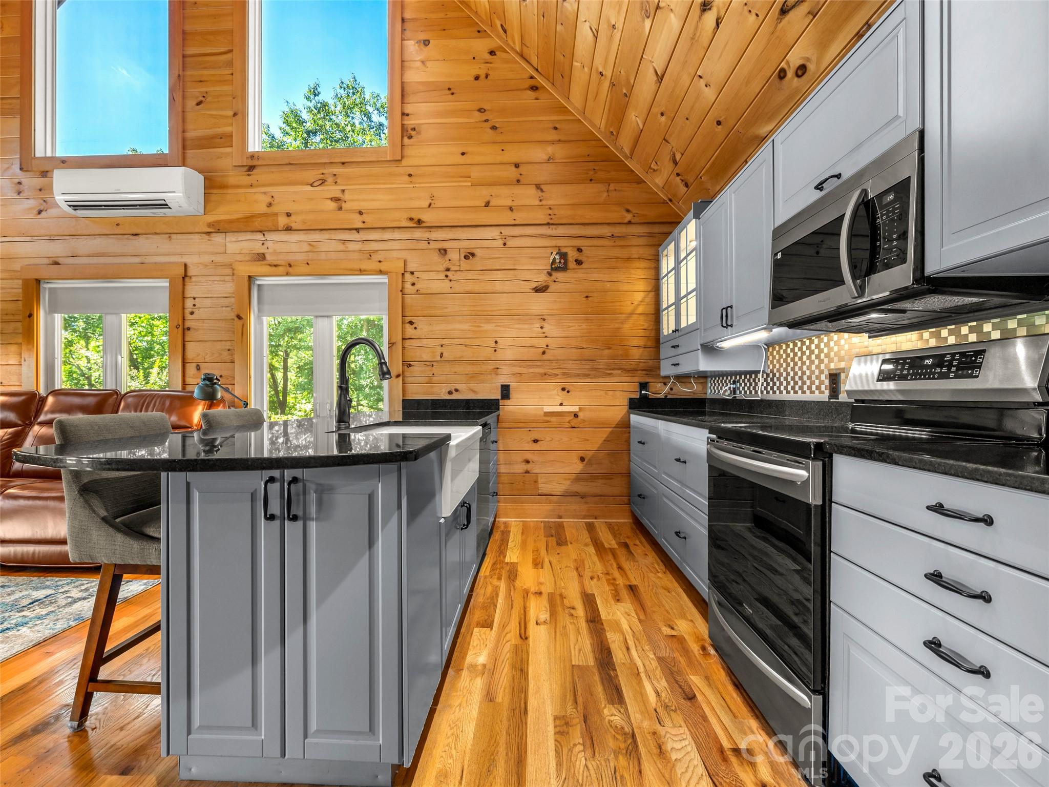 Wood-paneled kitchen with vaulted ceiling, gray cabinets, black countertops, and stainless steel appliances.