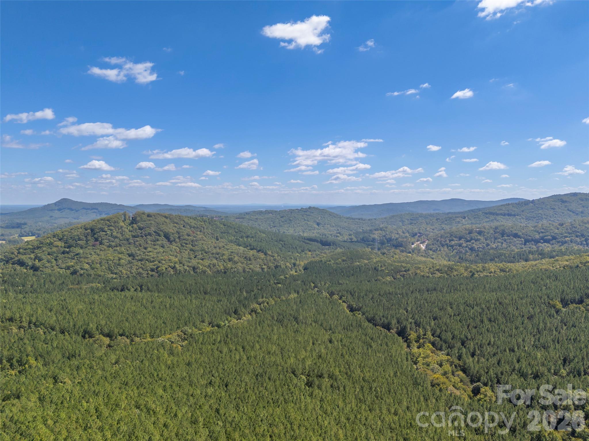 Aerial view of wooded mountain ridges stretching to the horizon beneath a blue, cloud-dotted sky.