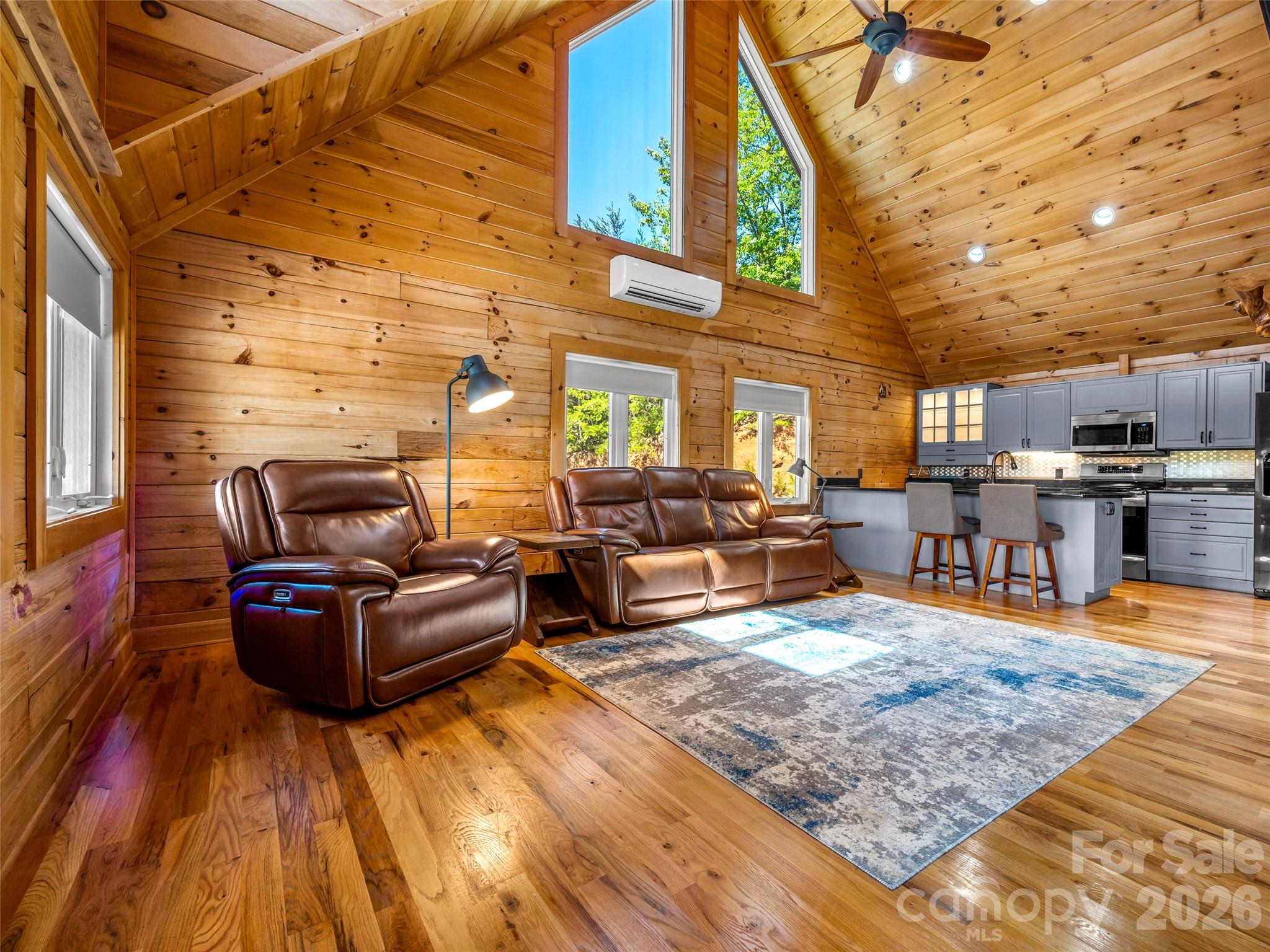 Wood-paneled living room with vaulted ceiling, leather recliners, and an open kitchen.