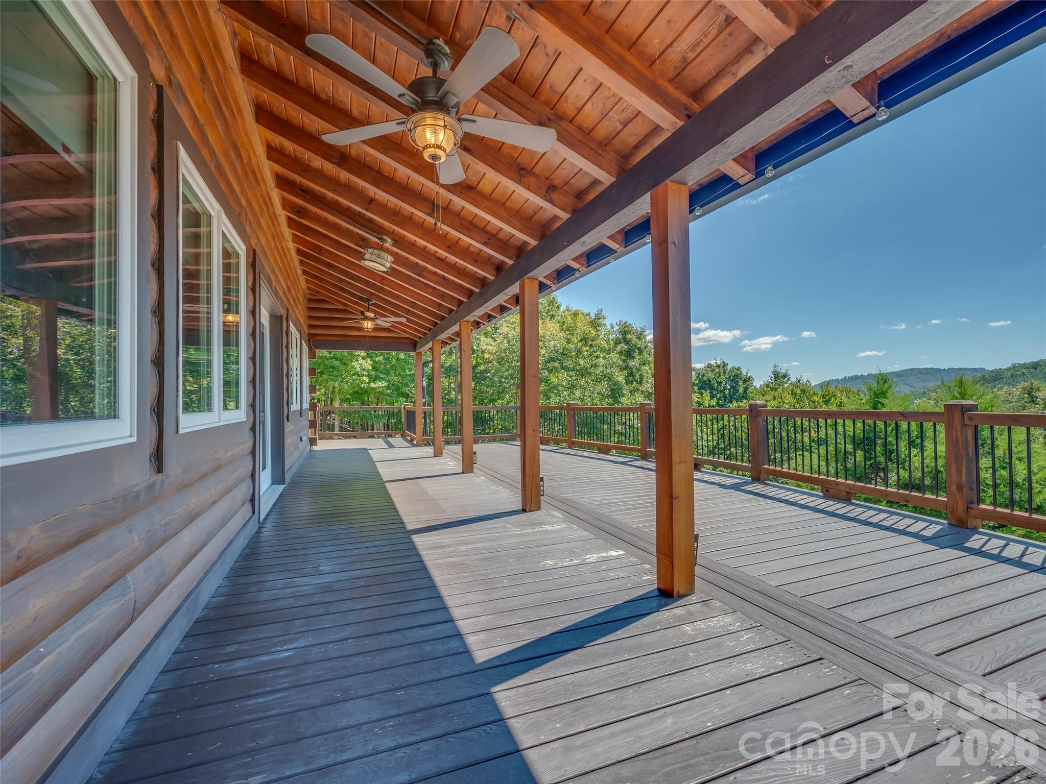 Covered wooden deck with ceiling fans and a wooded mountain view.