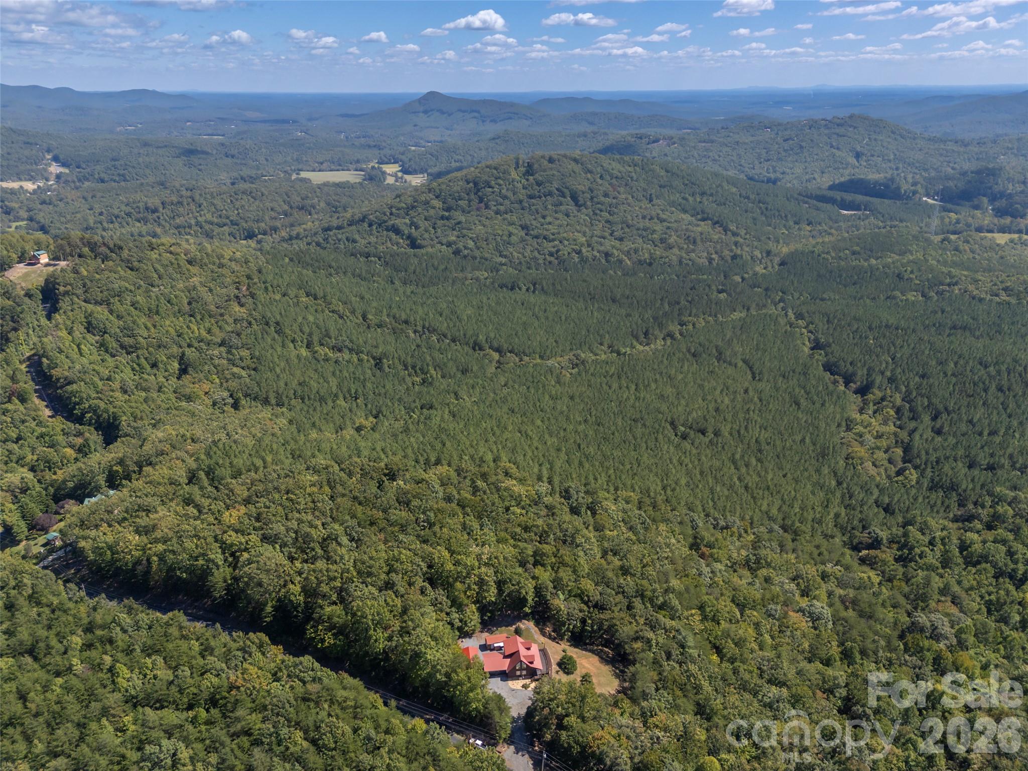 Aerial view of a red-roofed home amid dense forest, with mountain ridges stretching into the distance.