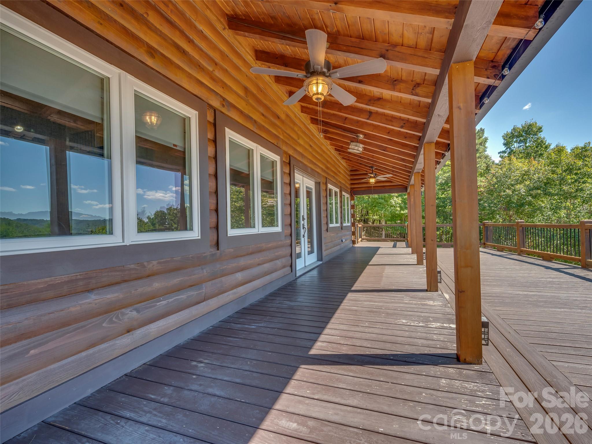 Covered wooden deck beside a log-sided home, with timber posts and mountain views reflected in the windows.